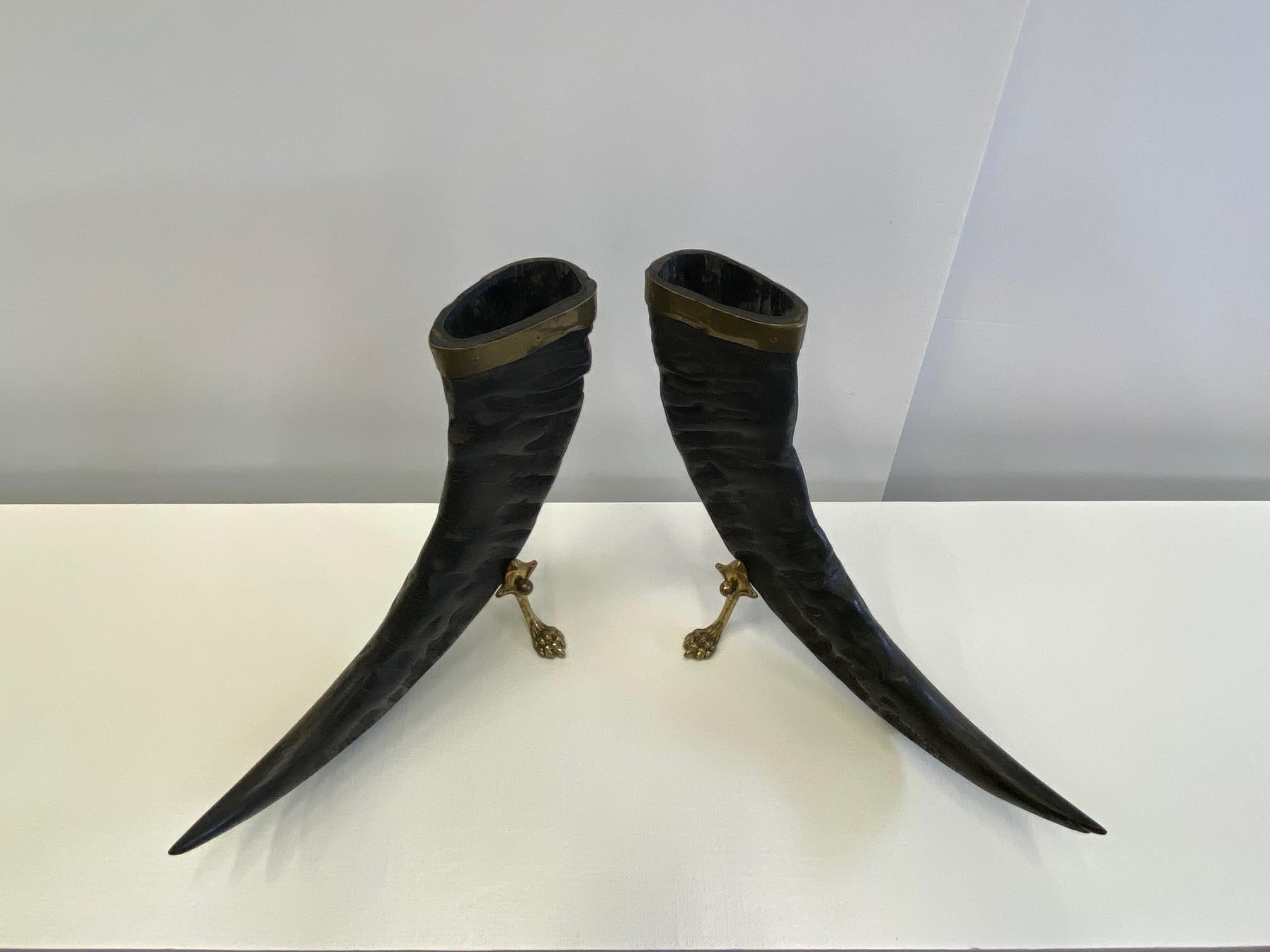 A fabulous pair of authentic sculptural buffalo horns having brass mounts around the tops and handsome brass bases with paw feet. An unexpected and beautiful masculine organic accessory.