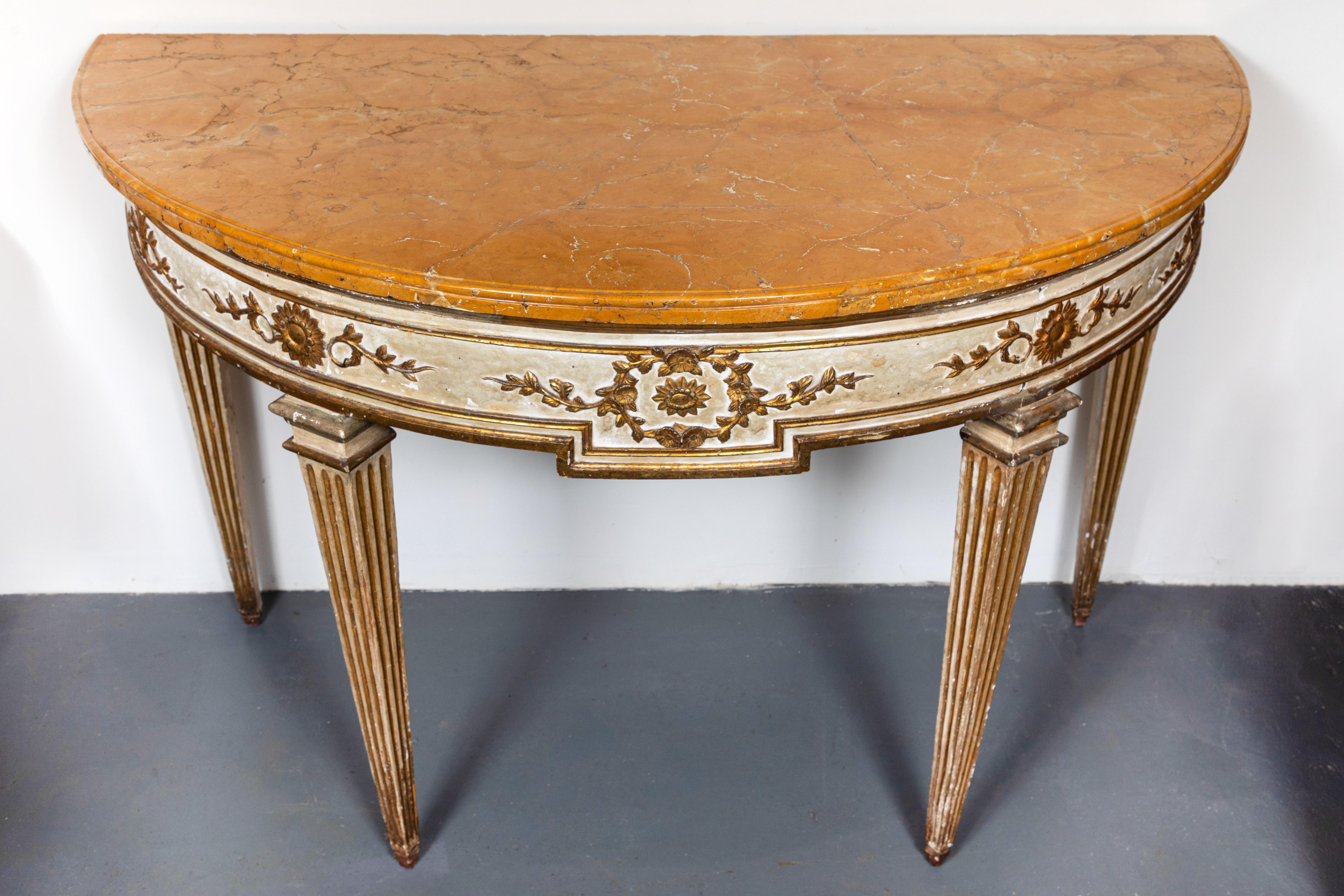 Pair of early 19th century, hand carved, painted and gilded, Italian neoclassical demilunes on fluted, tapered legs, surmounted by vibrant Siena marble tops. Each with aprons embellished with foliate vignettes and medallions.