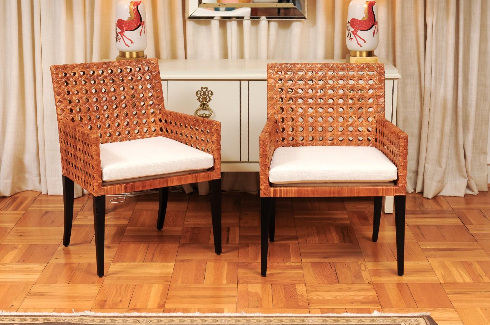 A stellar set of eight (8) elegant Organic cane arm chairs. Stout solid mahogany frame construction painstakingly veneered in hand-wrapped open French cane. Contrasting legs executed in dramatic black lacquer. The cane displays a rich warm Caramel