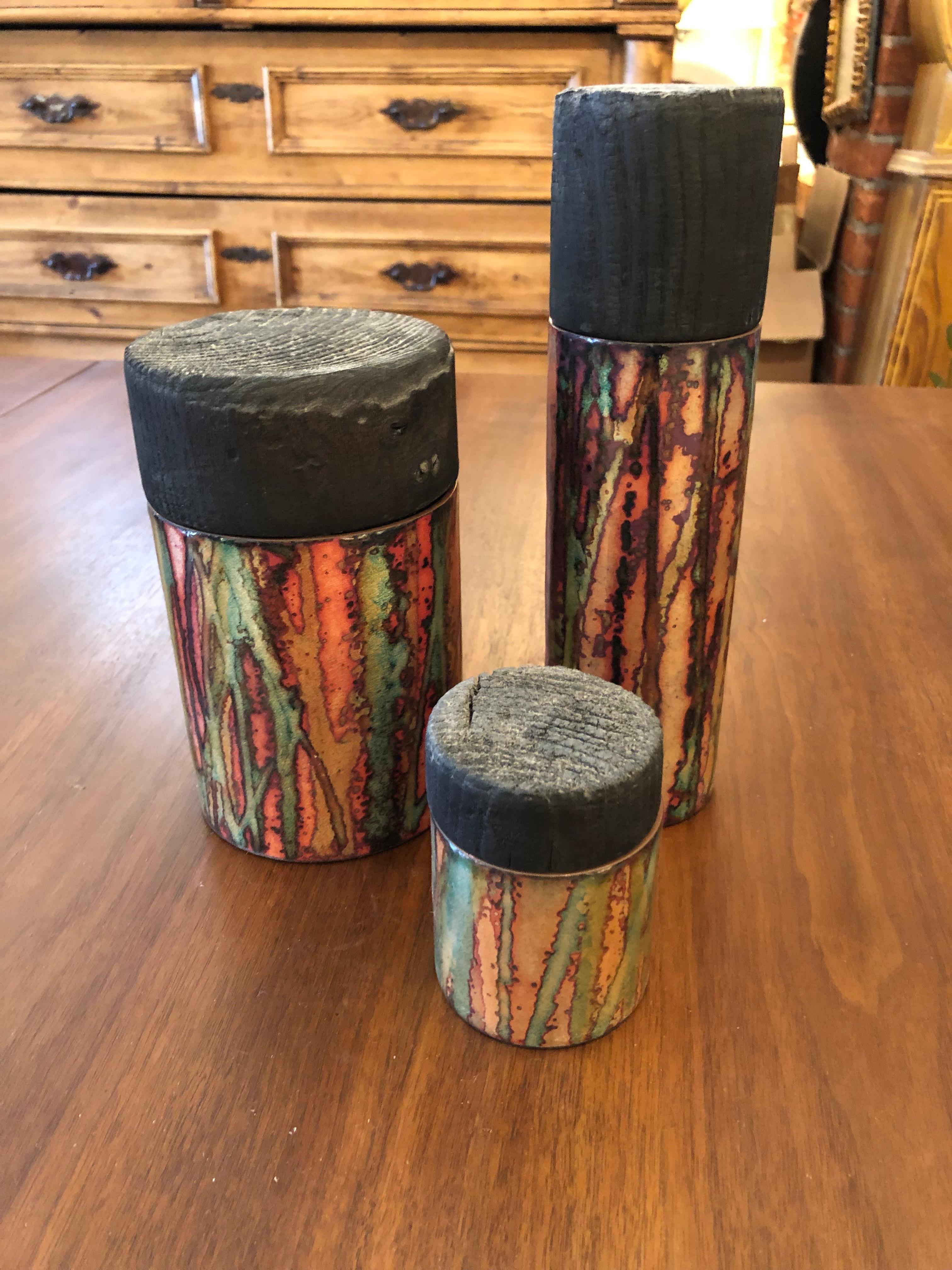 A striking artisan made set of 3 cylindrical copper cannisters having gorgeous shiny abstract glazing with marvelous irridescent oranges, greens, and purple.  The chunky tops contrast with the sleek shiny jars in their rustic matte forms, and are