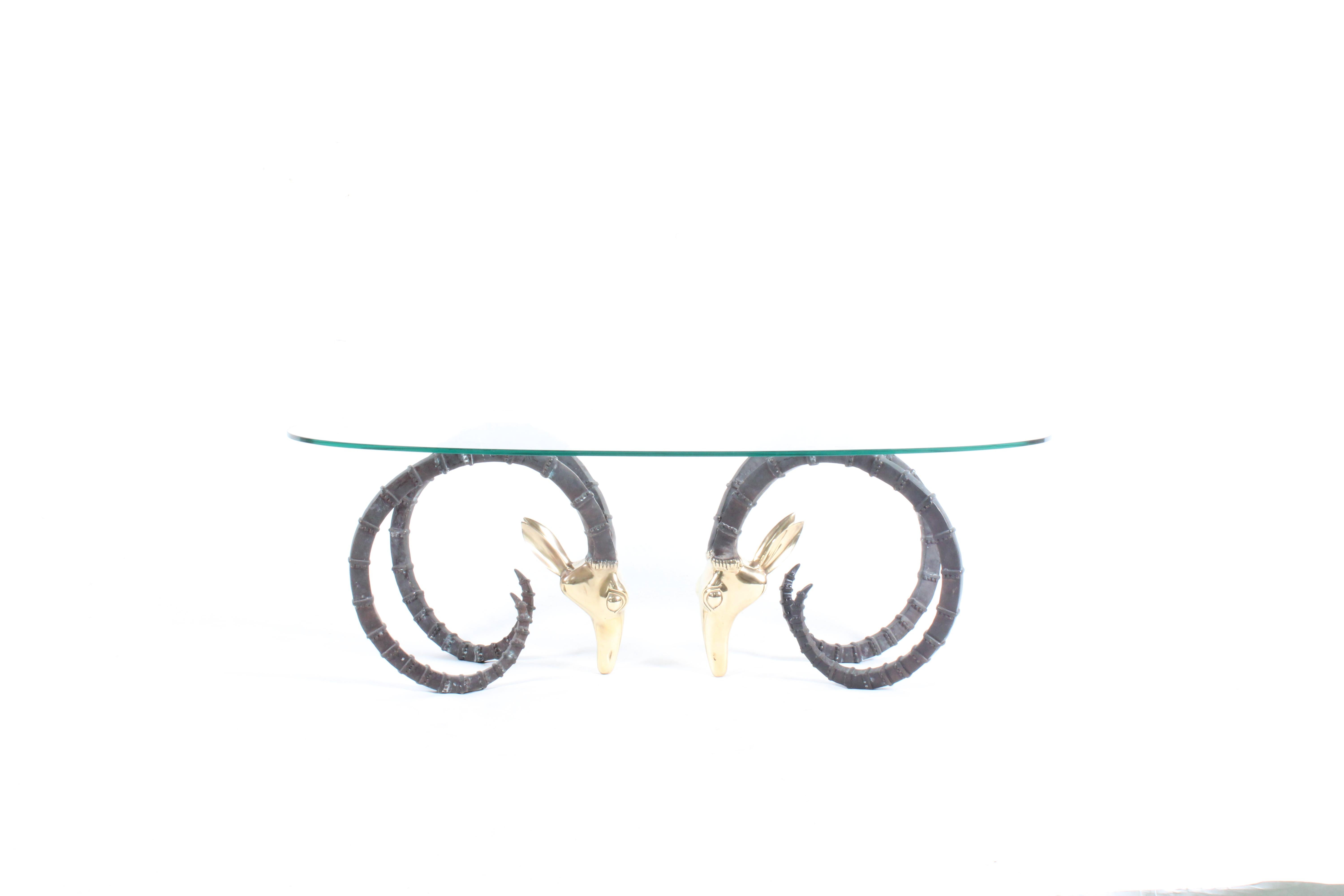 A stunning piece combing two vintage sculptural ibex or rams brass head bases which have highly polished heads and contrasting matt black painted horns on top of which is set an eliptical tempered glass top. Sourced from a private collector in Paris