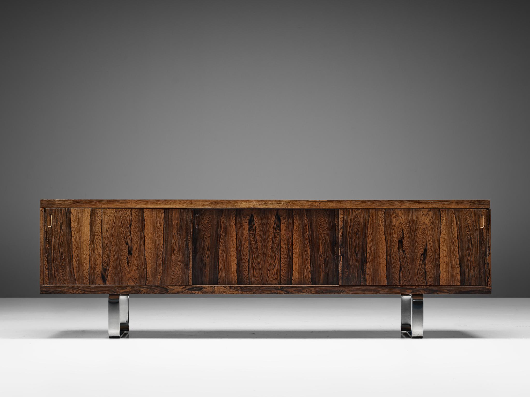 Credenza, bookmatched rosewood veneer, oak, and metal, Europe, 1960s. 

This striking sideboard is modest in its appearance yet highly well crafted. Behind the three sliding doors two shelves and a drawer unit executed in walnut are hidden.