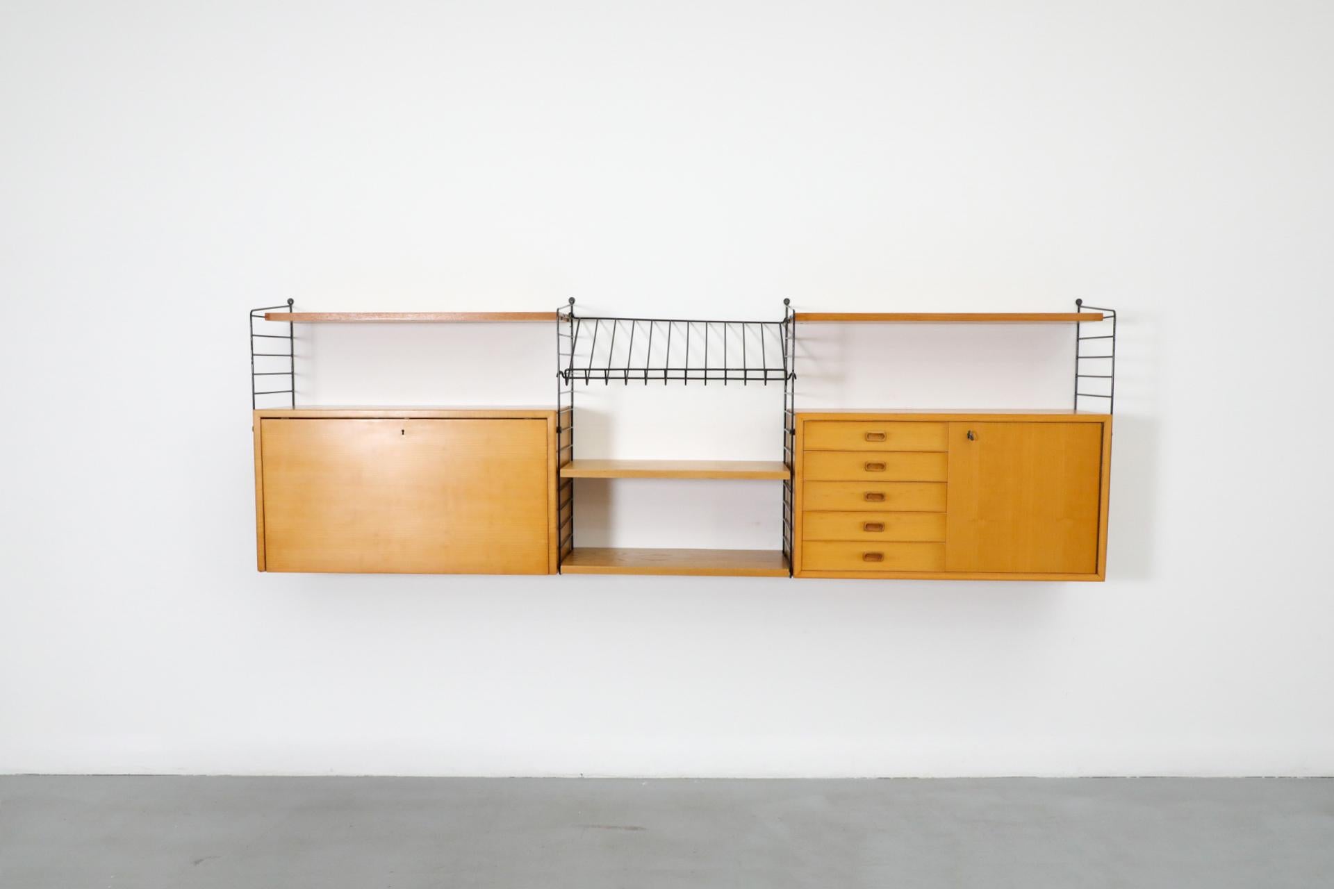 Beautiful Nils Strinning 3 section oak wall mount system with 4 shelves, two cabinets and a magazine rack with black enameled metal risers. This unit has one cabinet with drop down locking door and a glass shelf, the other has drawers, and a locking