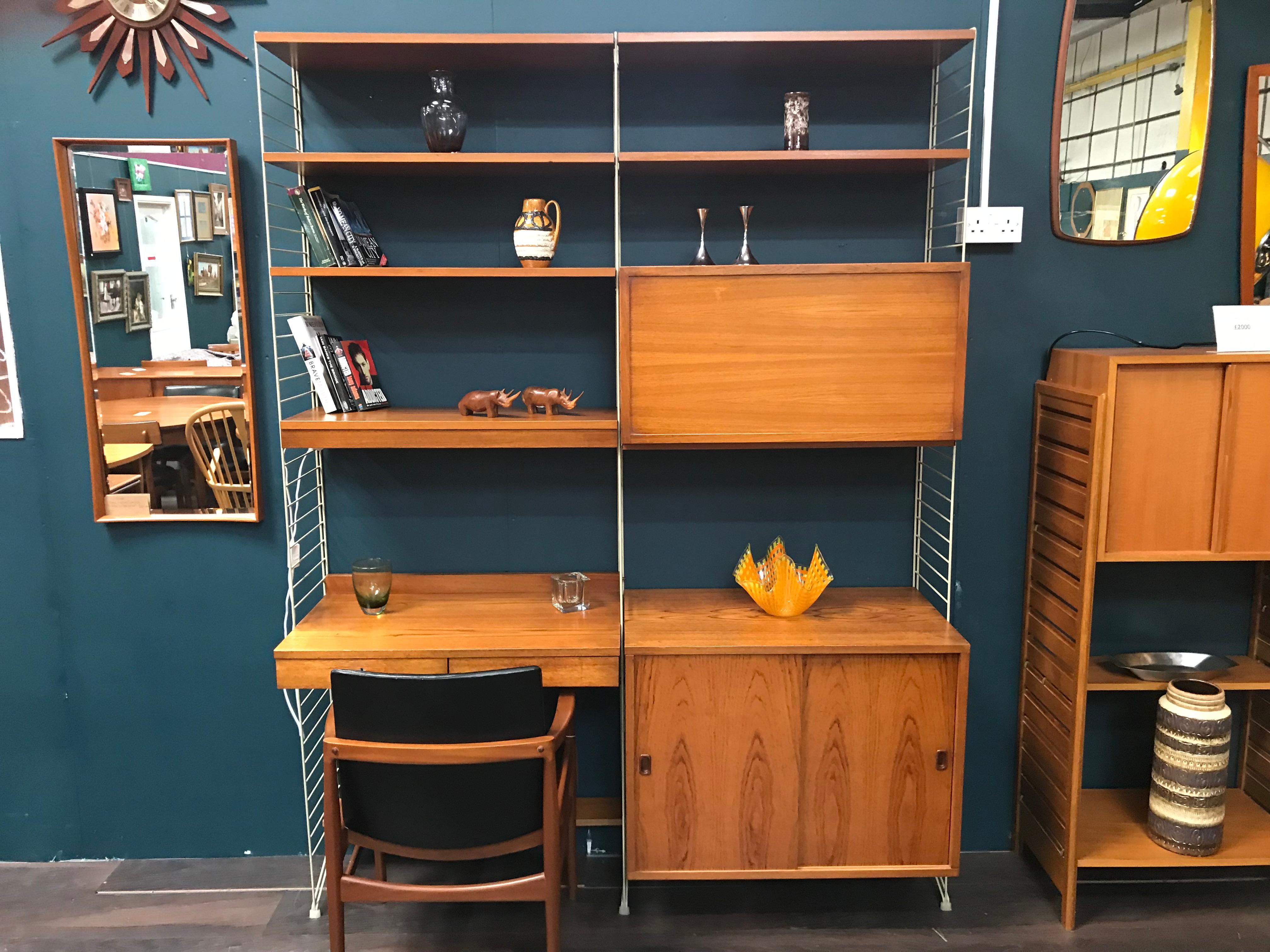 Stylish and functional, this is a Classic midcentury String shelving system designed by the Swedish designer Nils Nisse Strinning. The upright ladders allow the teak cabinets and shelves to be positioned wherever required. This is a very versatile