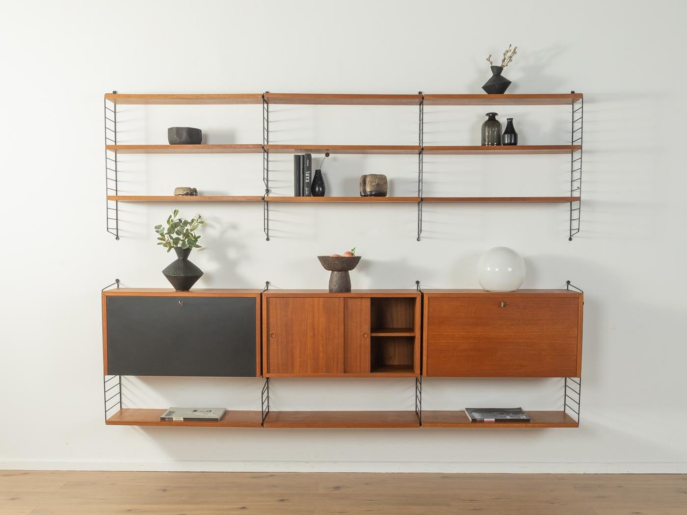 Scaffale originale String disegnato nel 1949 da Nils Strinning in impiallacciatura di teak. Il sistema è composto da dieci scale in metallo di colore nero con dodici ripiani, due contenitori con ante a battente e un contenitore con ante scorrevoli.