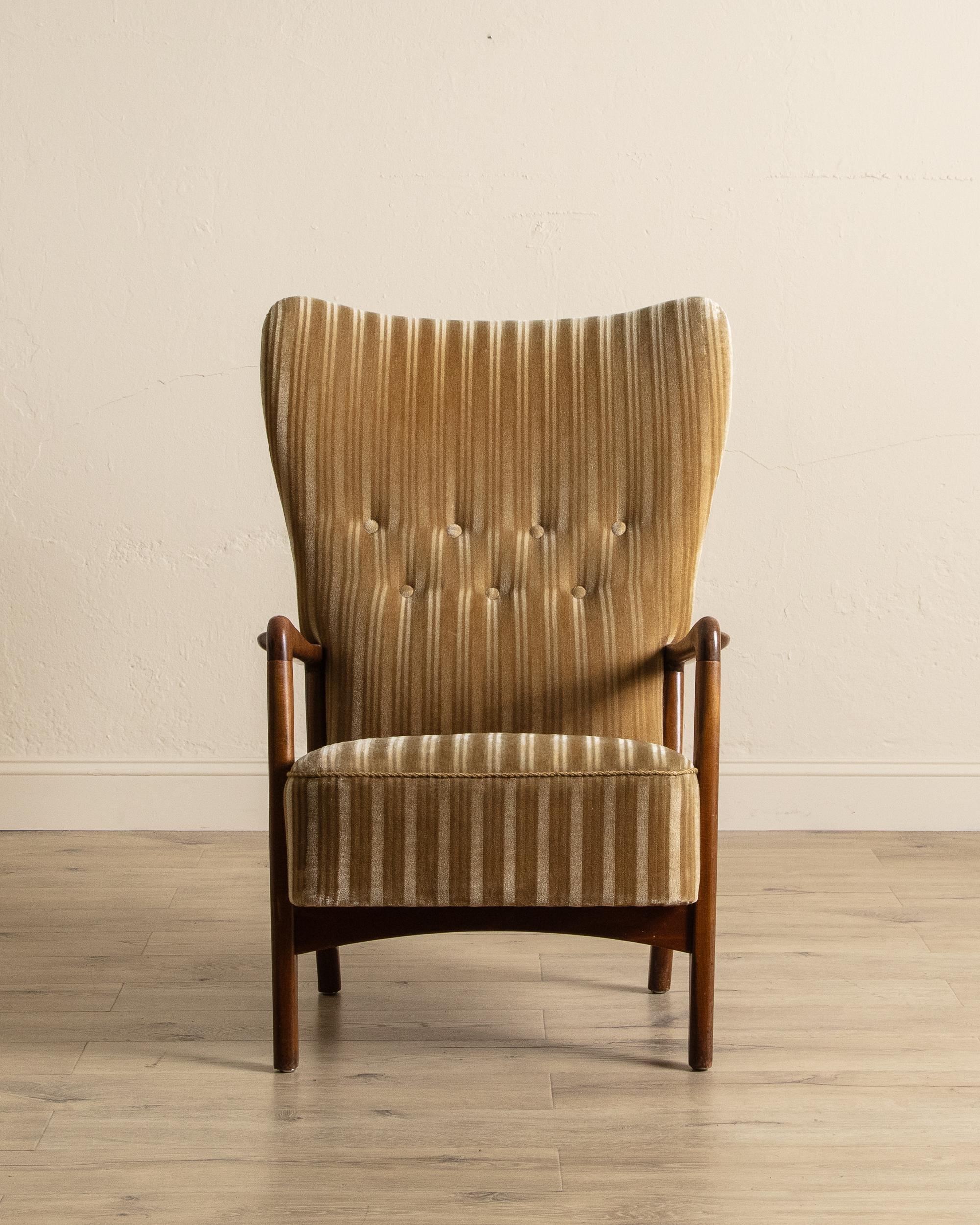 Cette chaise longue à haut dossier du milieu du siècle allie une forme sculpturale à un confort discret. Le dossier haut et ailé, avec ses courbes douces et ses capitons, offre à la fois un soutien et une silhouette accueillante, tandis que le