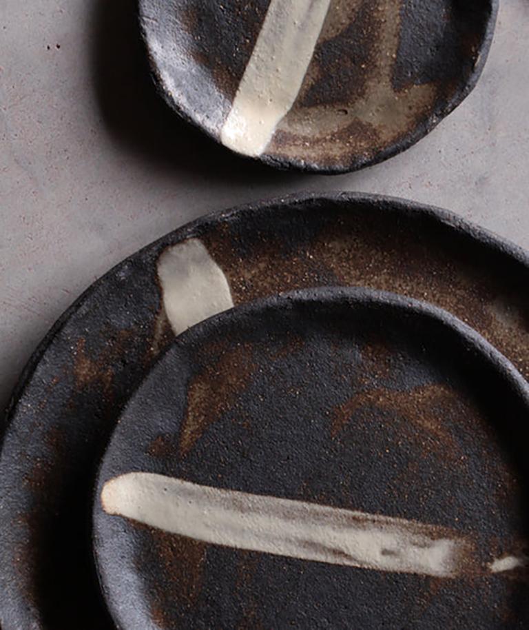 Set of dinnerware in black stoneware, featuring a hand-painted white stripe, entirely made and decorated by hand, covered with a transparent matte glaze. Each piece is shaped one by one, by hand, in the artist's studio located near Bordeaux, France.
