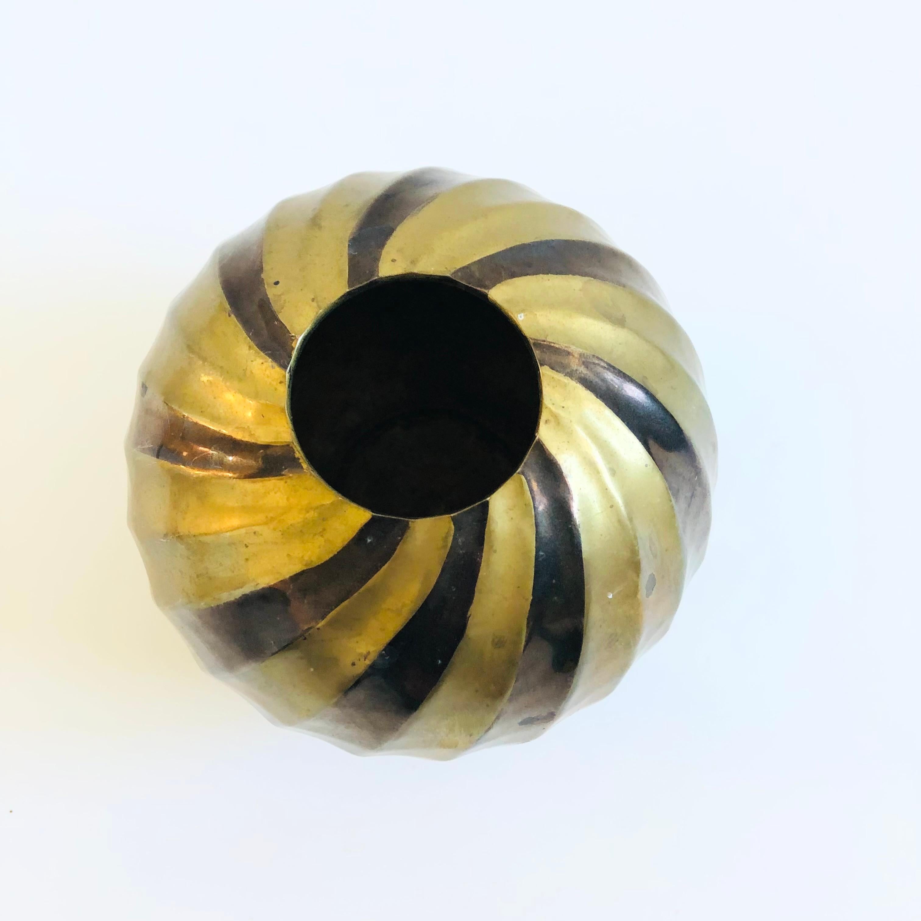 Un vaso vintage in ottone con un disegno in rilievo sulla superficie. La forma e i dettagli della sfera sono incantevoli, con bande intercambiabili di ottone dorato brillante e ottone patinato più scuro.


