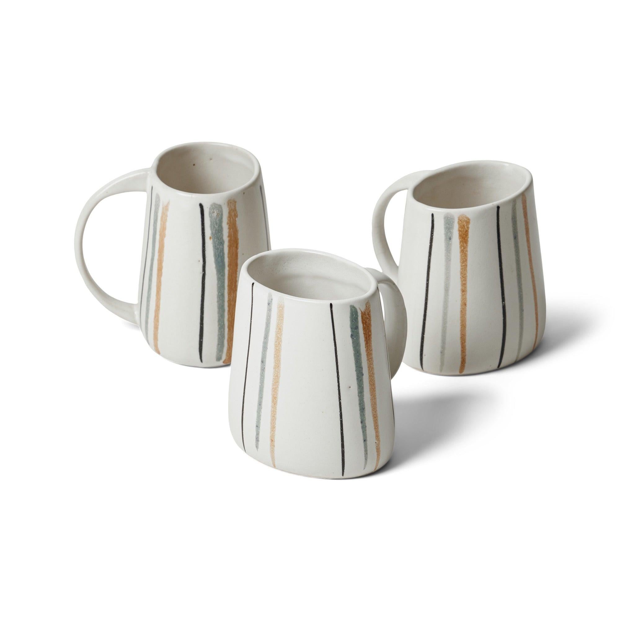 Mug en céramique de forme ovale avec poignée. Finition avec une glaçure blanche et des rayures turuoises, noires et beiges peintes à la main.