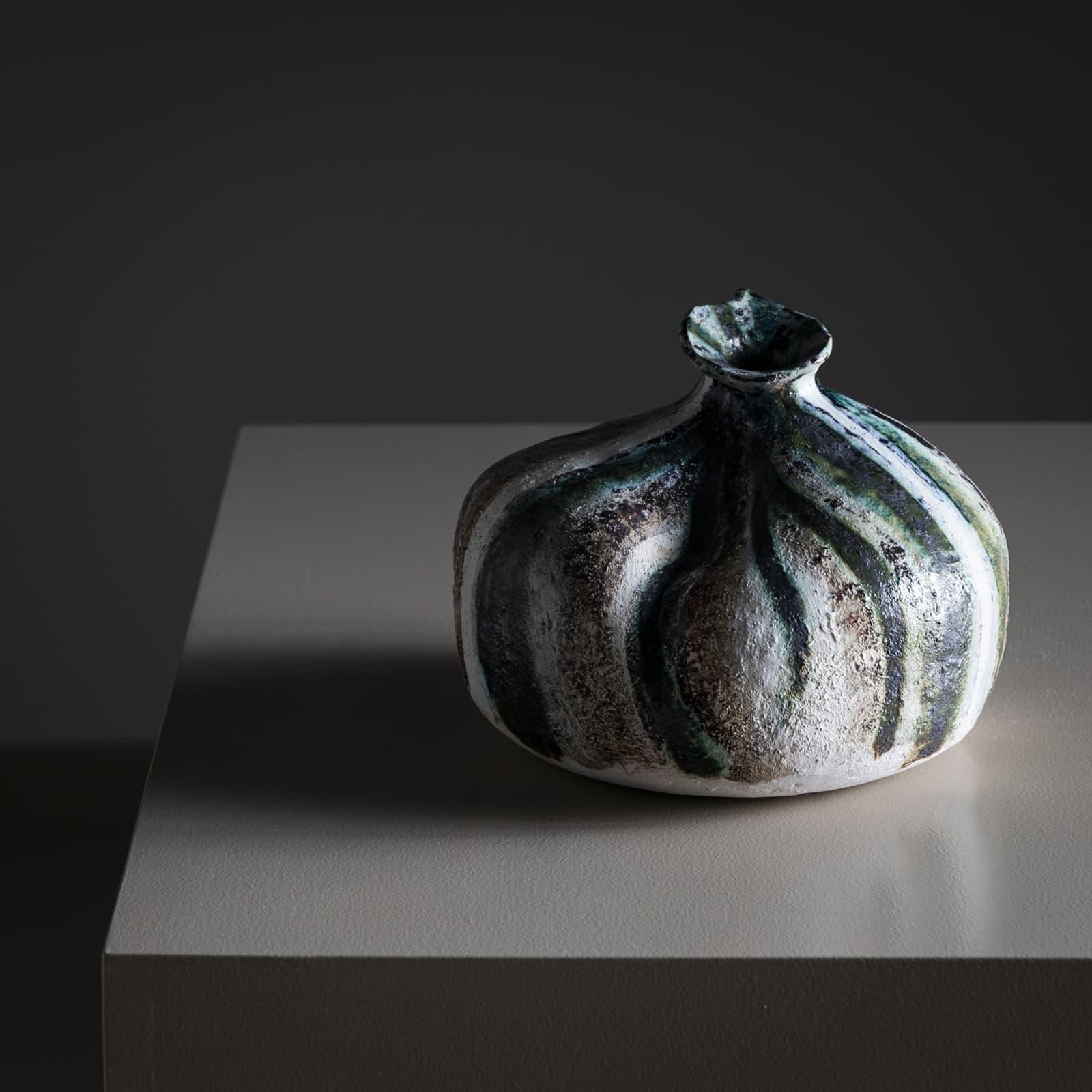 Vase en céramique en forme de gourde rayée avec glaçure verte, blanche, noire et brune et texture légèrement irrégulière. Le vase est signé POEMU sur la base.

Poemu est un artiste français pluridisciplinaire connu pour sa créativité dynamique qui