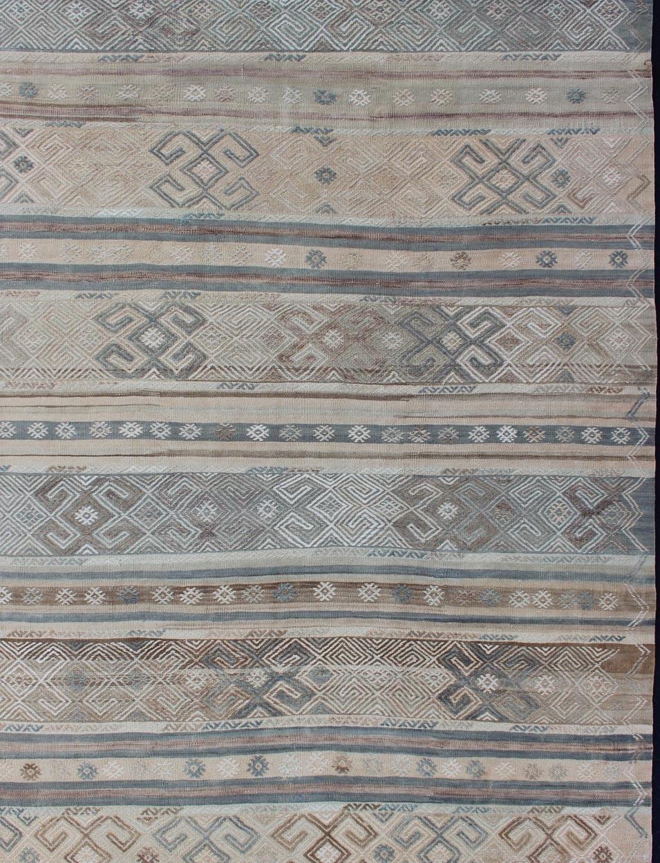 Measures: 5'9 x 7'7.

This flat-woven Kilim from Turkey features an enticing composition consisting of stripes with fascinating geometric designs rendered in natural tones of brown and gray, as well as some blue shades. 

Vintage Kilim with Stripes