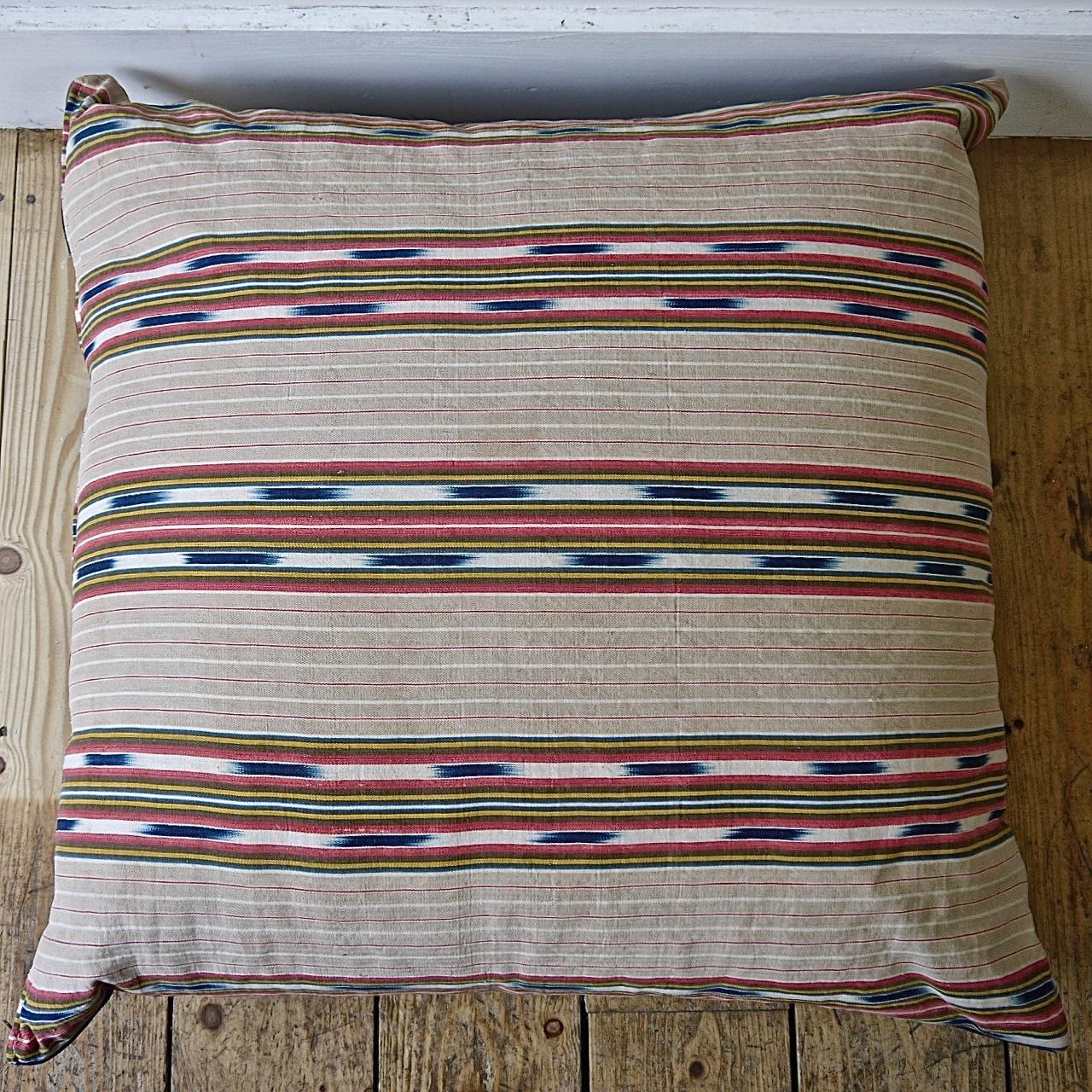 Late 19th century French floor cushion made from an interesting and unusual striped linen/cotton ticking with an indigo ikat detail. Stripes of faded beige, red and yellow with the indigo ikat floating in between. Backed in a vintage denim cloth