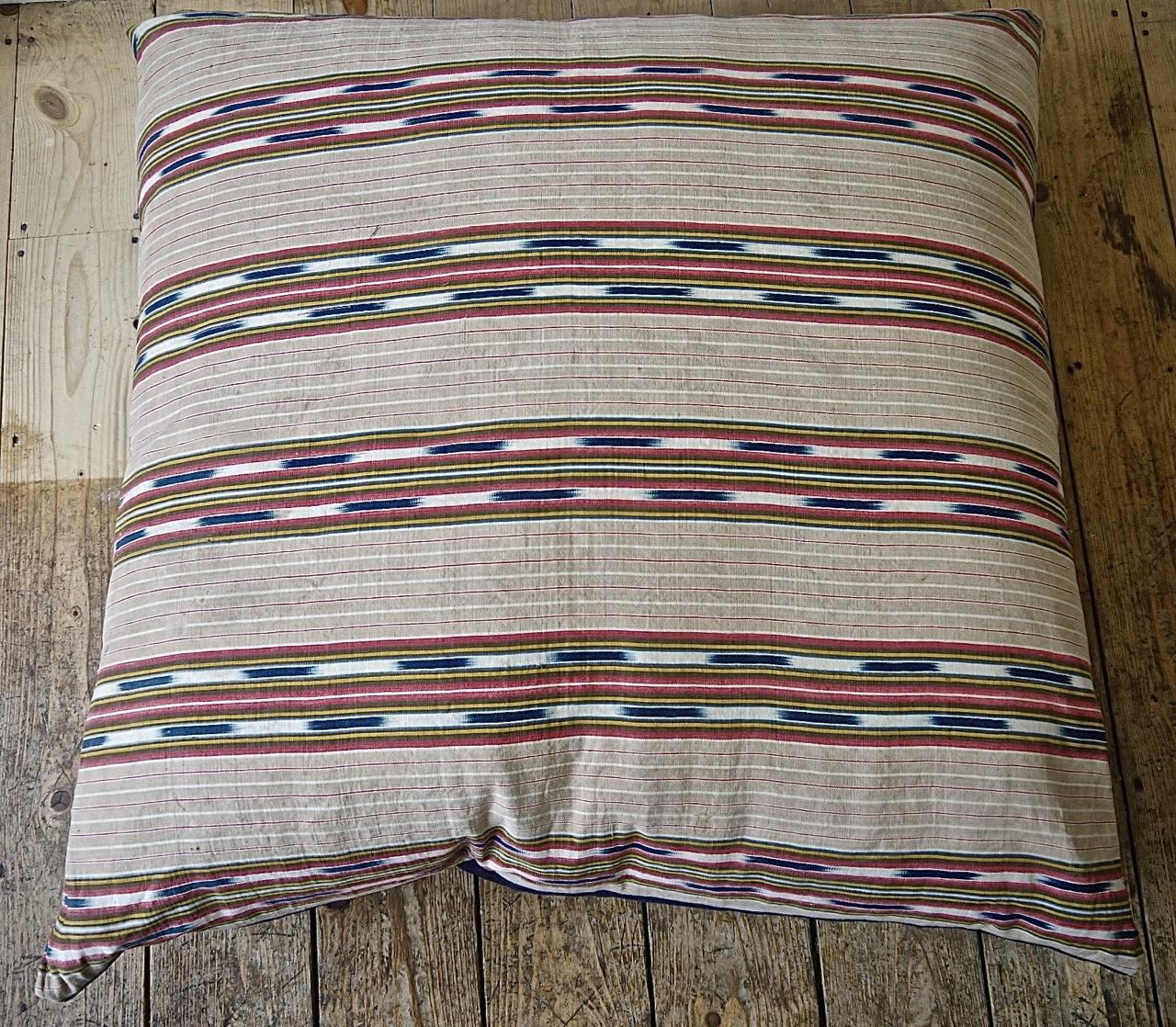 Late 19th century French floor cushion made from an interesting and unusual striped linen/cotton ticking with an indigo ikat detail.Stripes of faded beige, red and yellow with the indigo ikat floating in between.Backed in a vintage denim cloth with