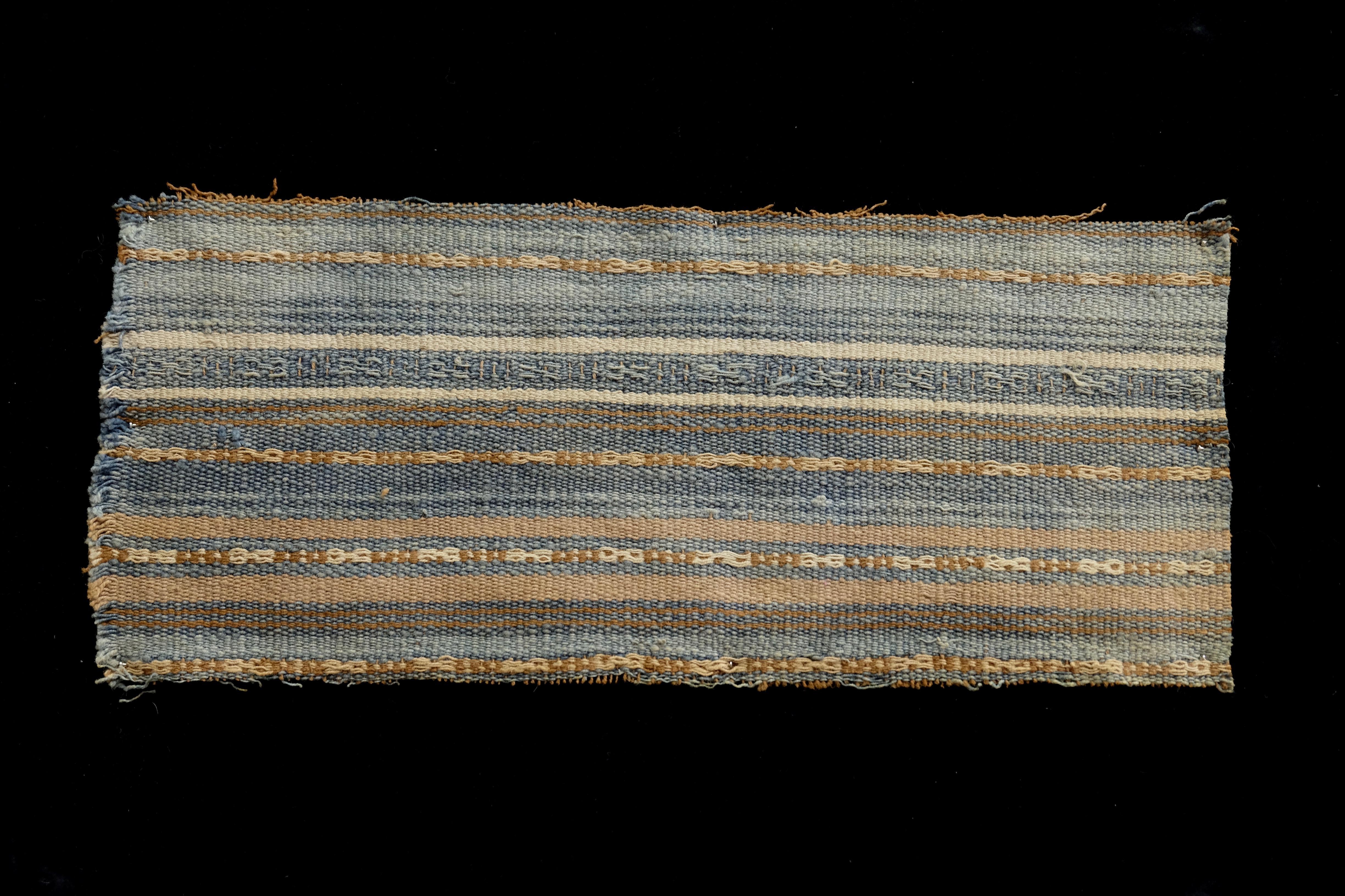 Hues of blue and brown adorn this minimalist pre-Columbian textile fragment in striped pattern. this piece is mounted in a black shadowbox frame. 

It is a wonder to behold antiquities such as a pre-Columbian textiles, an authentic piece of art