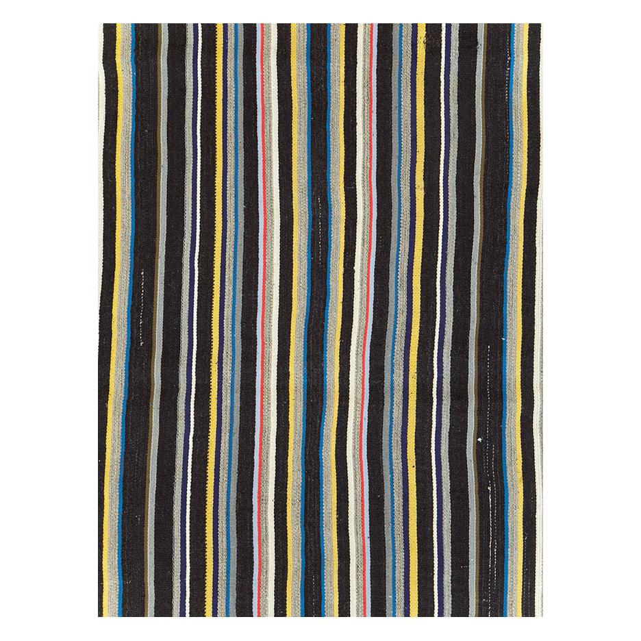 A vintage Turkish flatweave Kilim room size carpet handmade during the mid-20th century with a vertically striped multicolored pattern including shades of black, red, blue, and yellow.

Measures: 9' 7