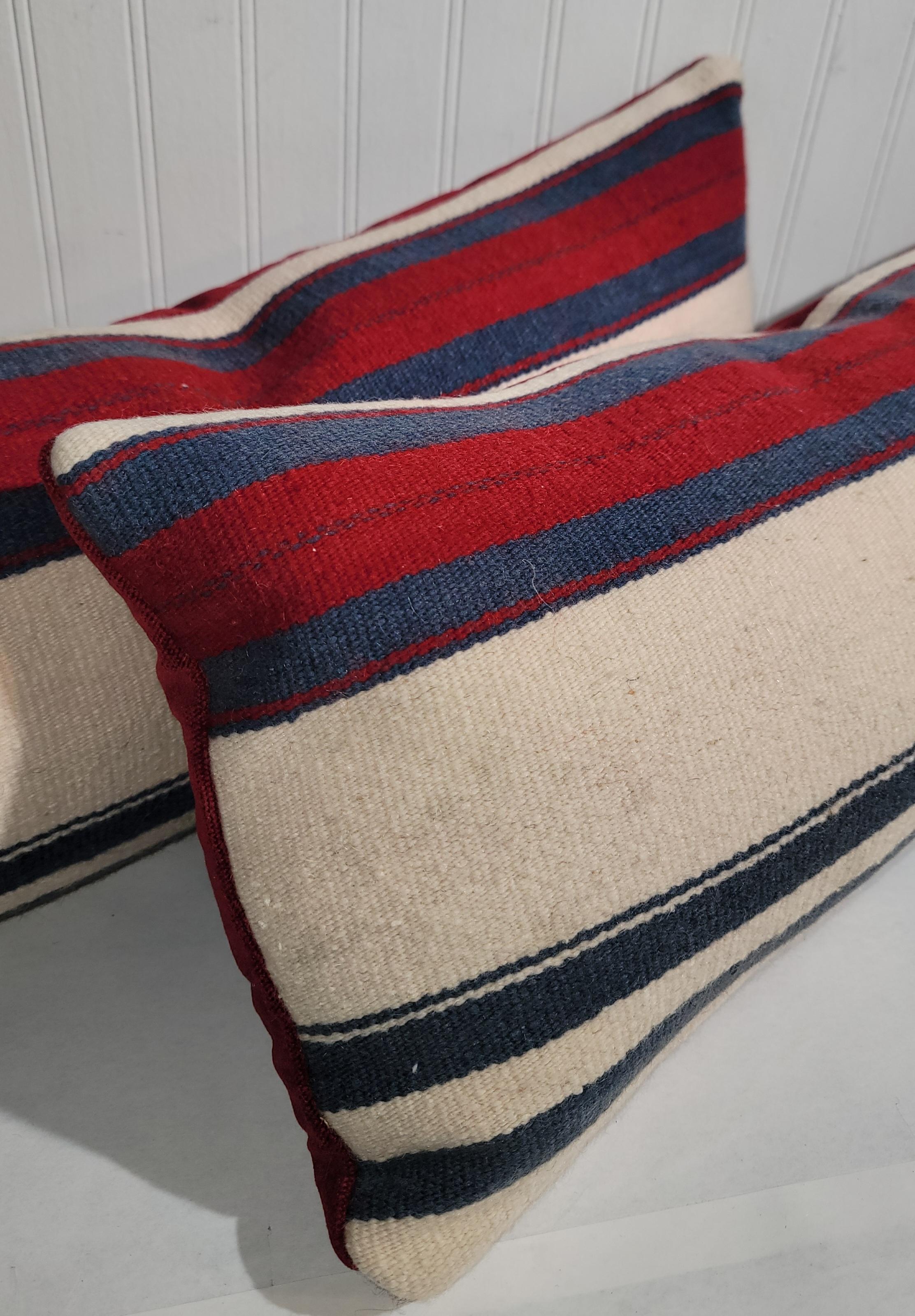 Cuscini messicani in lana serape a righe colorate. I rossi e i blu brillanti offrono un'ottima palette di colori su cui lavorare. Questi cuscini in lana per reni sono lunghi e hanno il retro in lino rosso. Gli inserti in piuma e piumino sono
