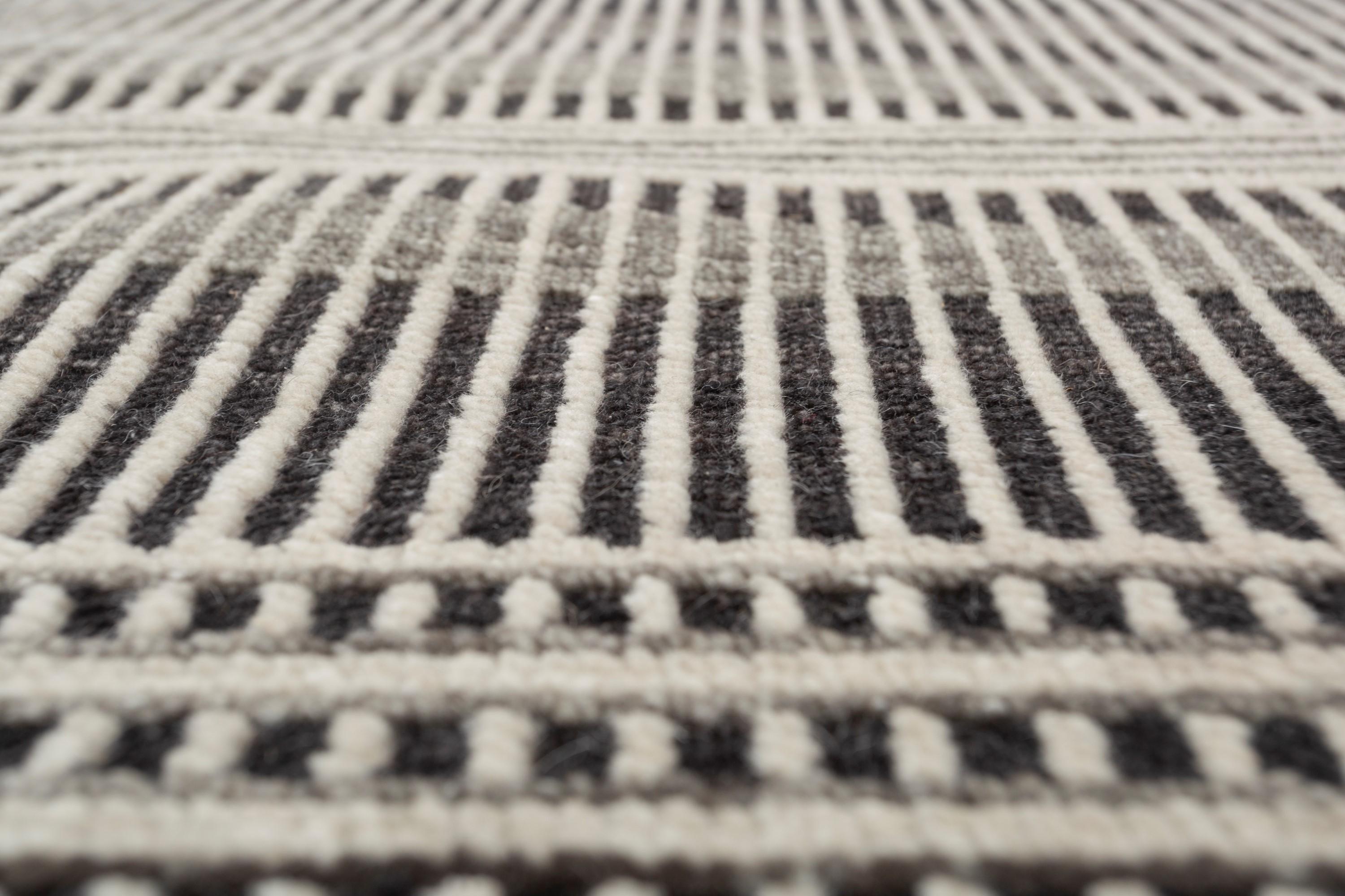 Con un juguetón juego de rayas de diferentes anchuras y profundidades, la moderna alfombra hecha a mano crea una ilusión visual dinámica y cautivadora. Las rayas transitan sin interrupción a través de un sutil efecto degradado, añadiendo profundidad