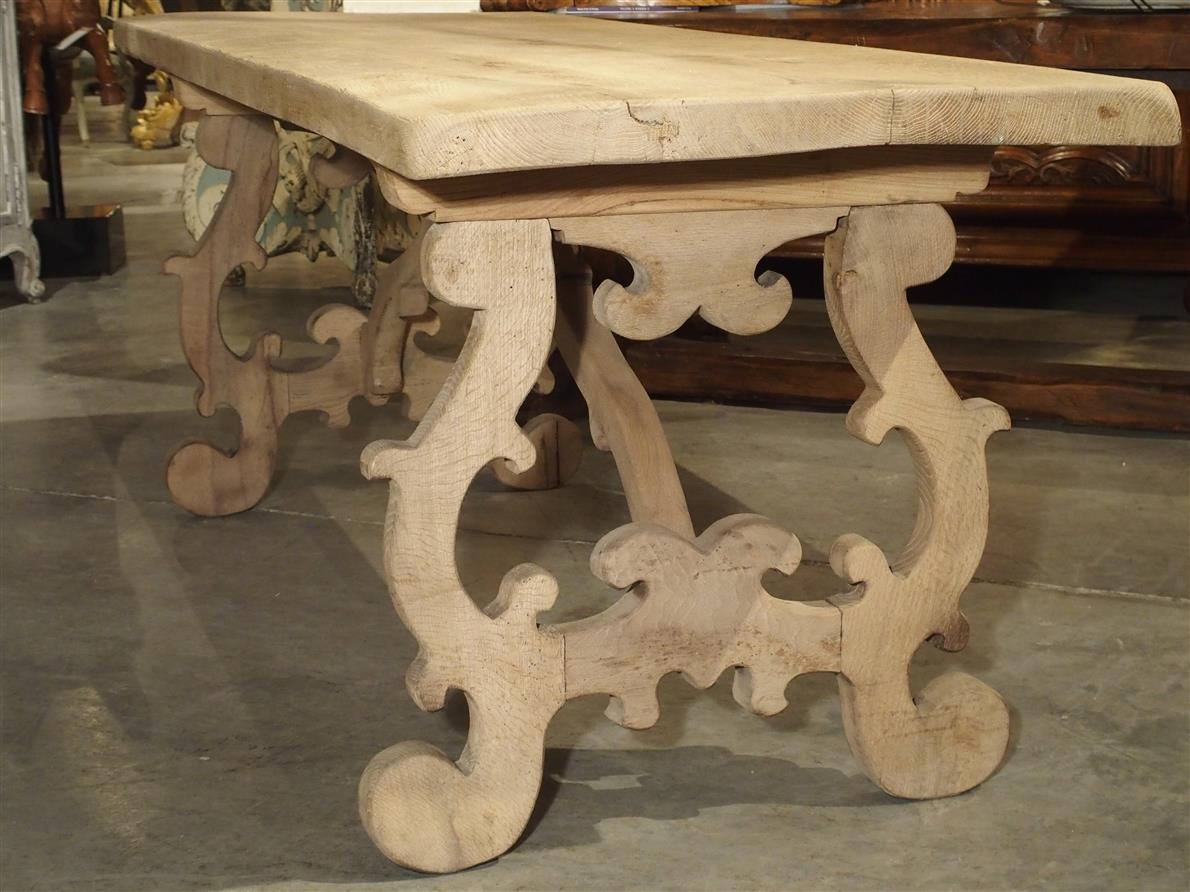 From Northern Italy, this stripped and bleached oak table has open lyre shaped legs on turned feet at either end. There are shaped wooden stretchers going from the center of the underside of the table to the center of the side stretchers. C-scroll