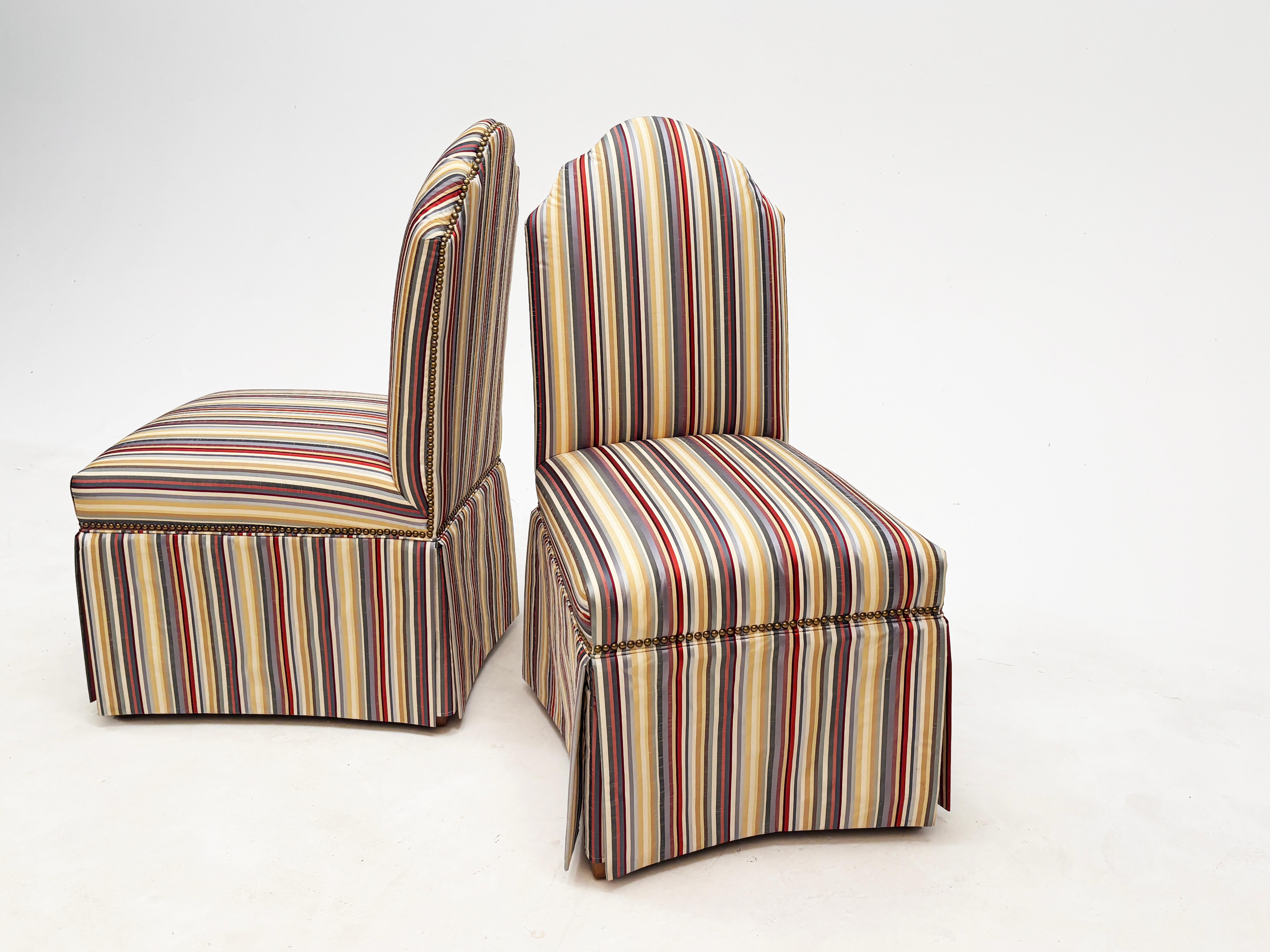 Questa splendida coppia di sedie a pantofola presenta uno schienale curvo unico nel suo genere, è rivestita in uno splendido tessuto Jacquard taffetà che sfoggia una tavolozza di creme, ori, blu, creme, verdi raccolti e rossi ed è rifinita con teste