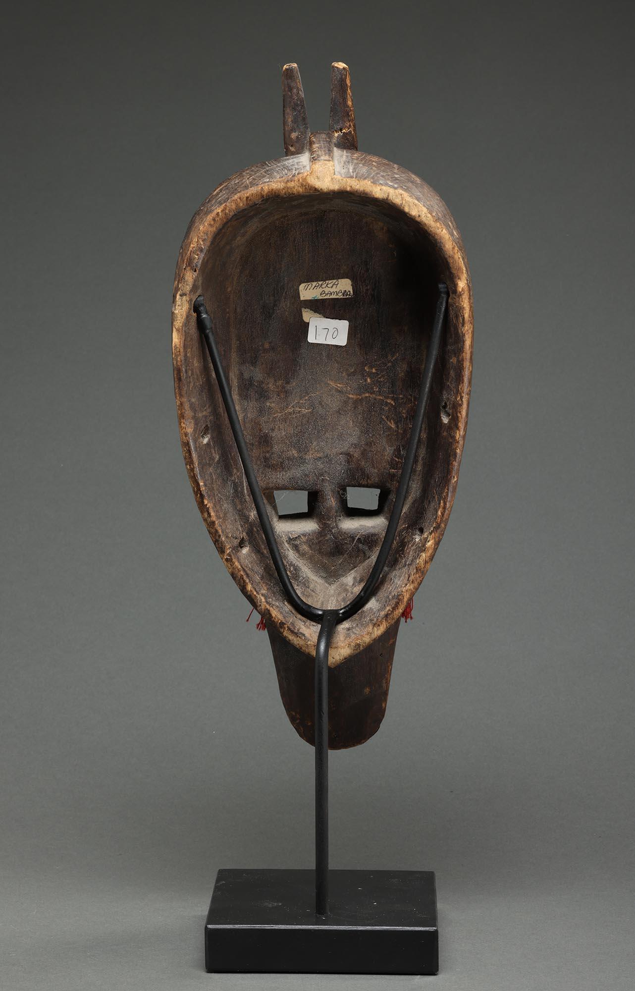 Starke Marka Antilope - menschliche Holzmaske mit Metall, Mali Afrika.  Große, quadratische, offene Augen, lange Nase mit waagerechten Lippen, drei vorspringende Metallzöpfe aus Messing, die mit gefiederten Stoffspitzen über dem Gesicht enden, zwei
