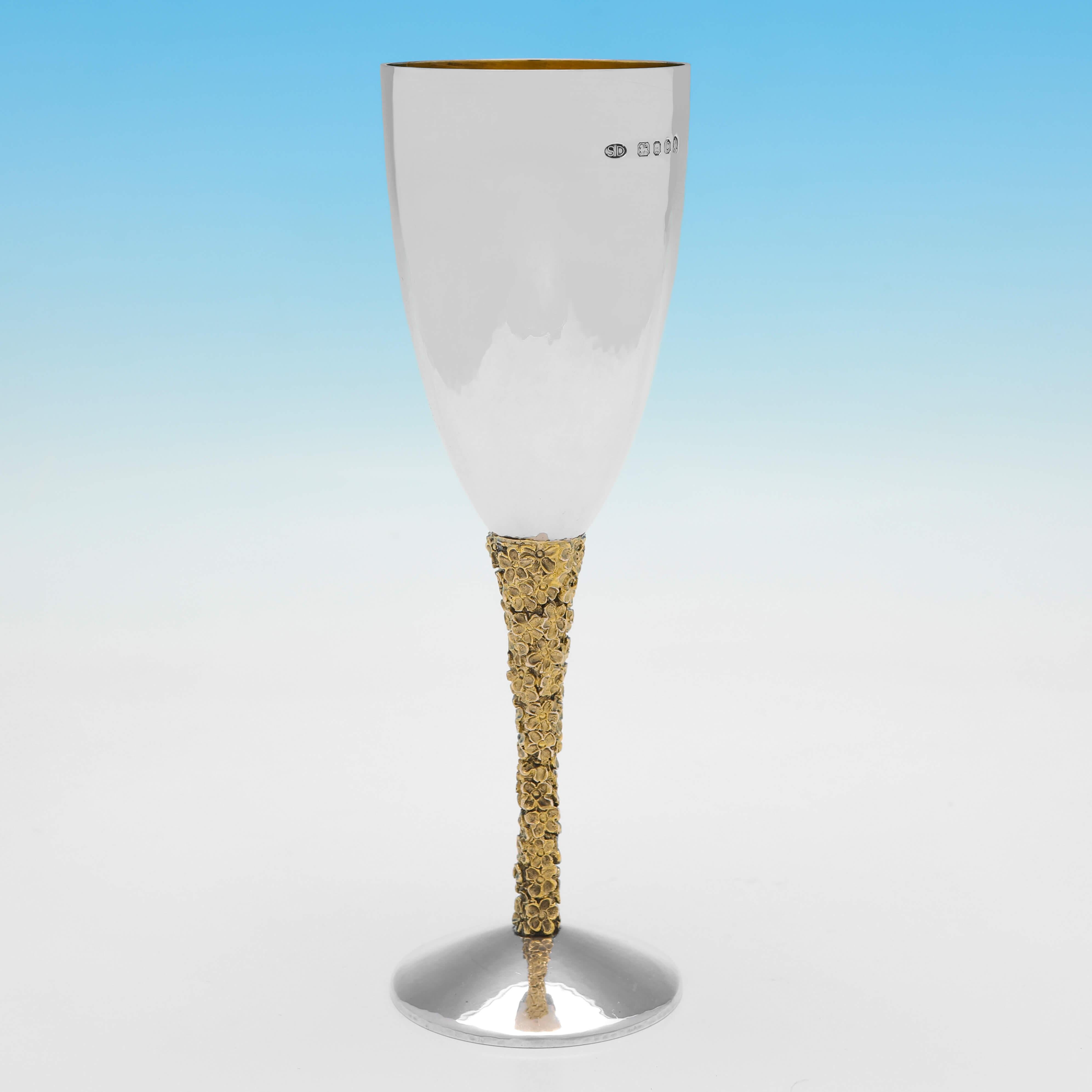 Hallmarked in London in 1977 by Stuart Devlin, this handsome pair of Sterling Silver Champagne Flutes, have cast and gilt floral head decoration to the stems, a hand hammered finish, and gilt interiors. 

Each champagne flute measures 7.5