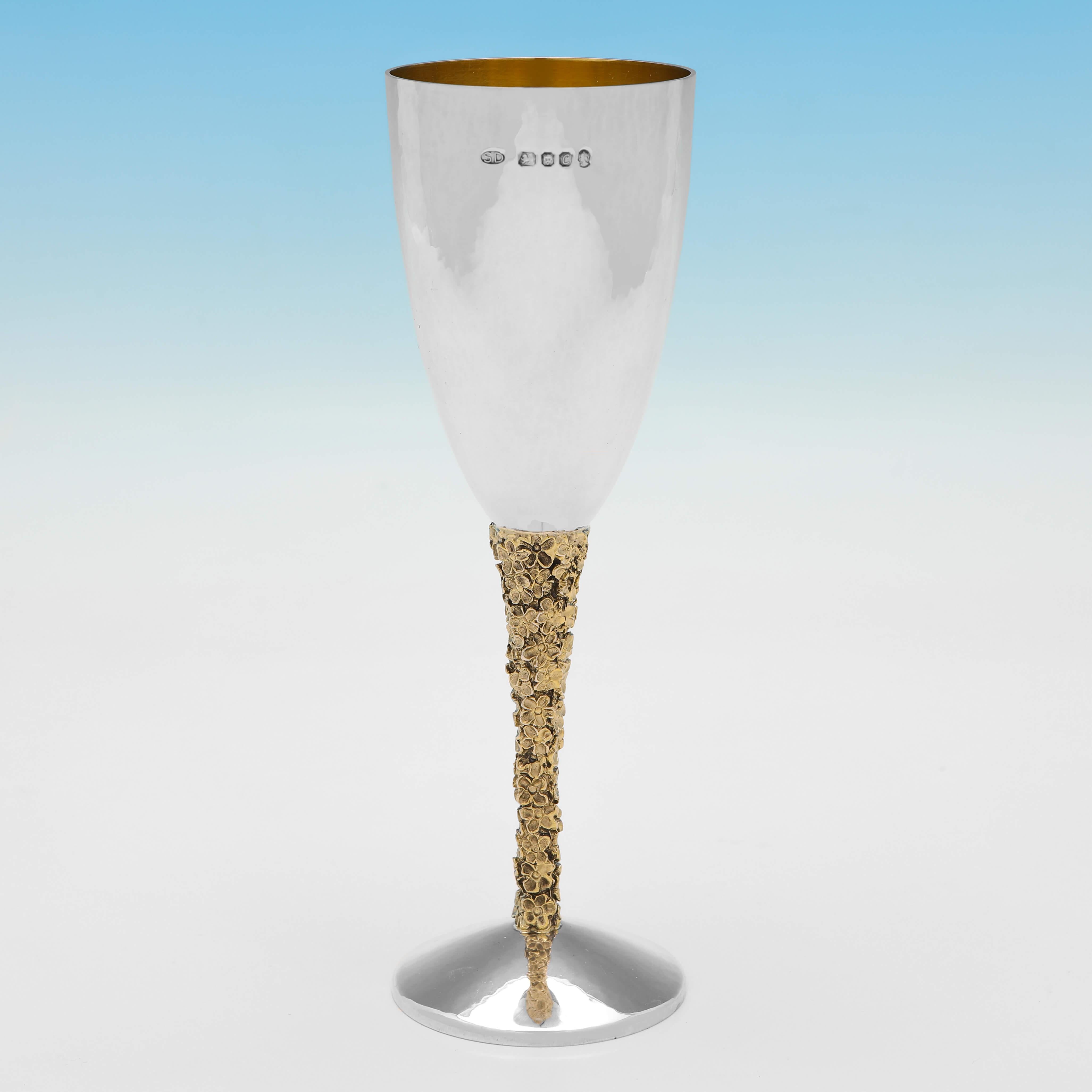Hallmarked in London in 1977 by Stuart Devlin, this handsome pair of Sterling Silver Champagne Flutes, have cast and gilt floral decoration to the stems, a hand hammered finish, and gilt interiors. 

Each champagne flute measures 7.5