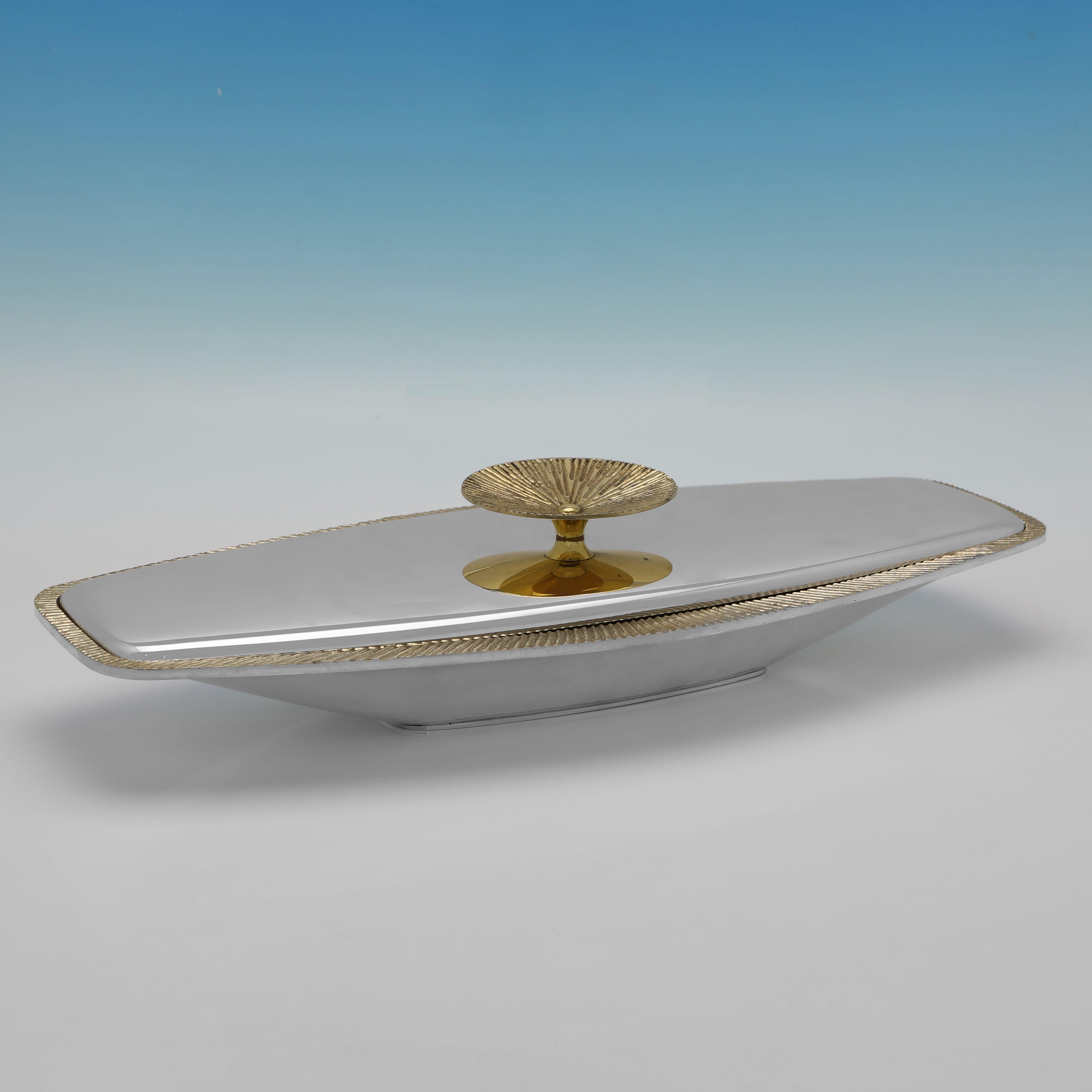 Matriculados en Londres en 1970 por Stuart Devlin, este maravilloso par de platos de entrante de plata de ley están bellamente diseñados, con bordes y asas dorados. 
Cada plato mide 7,5 cm de alto, 40 cm de ancho y 17 cm de fondo, y los dos juntos
