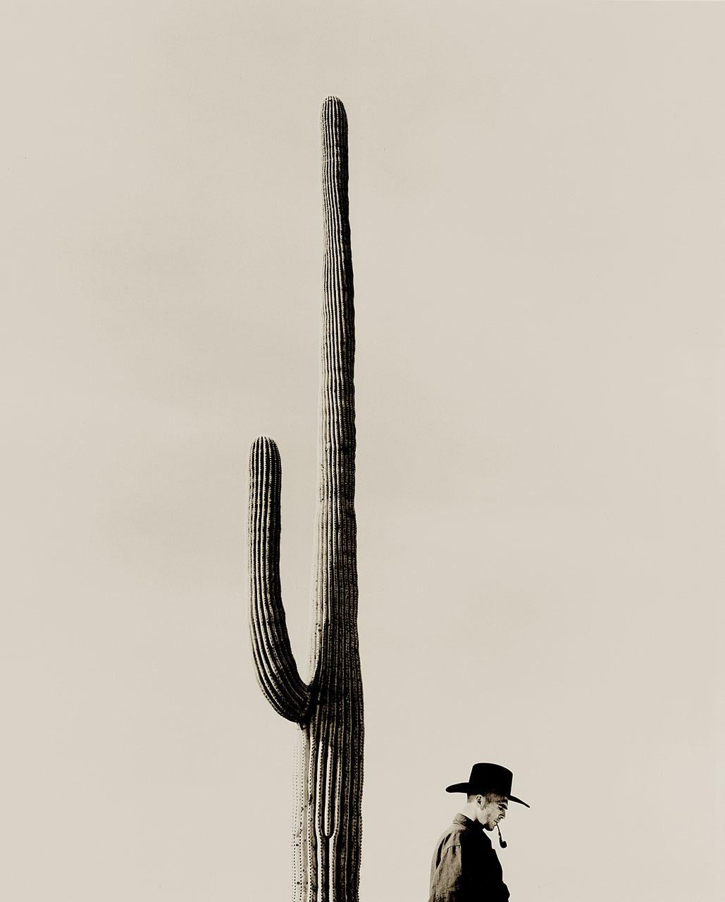 A cowboy in contemplative pose in front of a saguaro cactus.  The man is wearing a stetson hat and smoking a pipe.  The image evokes the solitude of life on the plains and seems to emphasize the sheer size of the environment. 

The saguaro is a