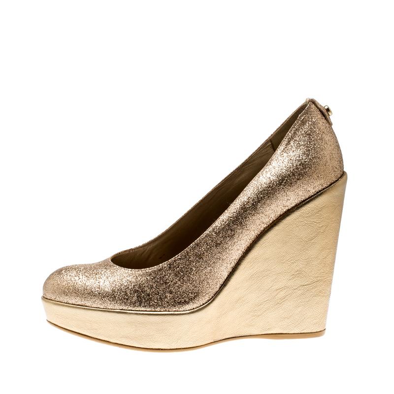 These Stuart Weitzman pumps will make sure you cruise in style all day long! The metallic gold pumps are crafted from glitter. They flaunt round toes and come equipped with comfortable insoles and 12 cm cork wedge heels. Pair them with your