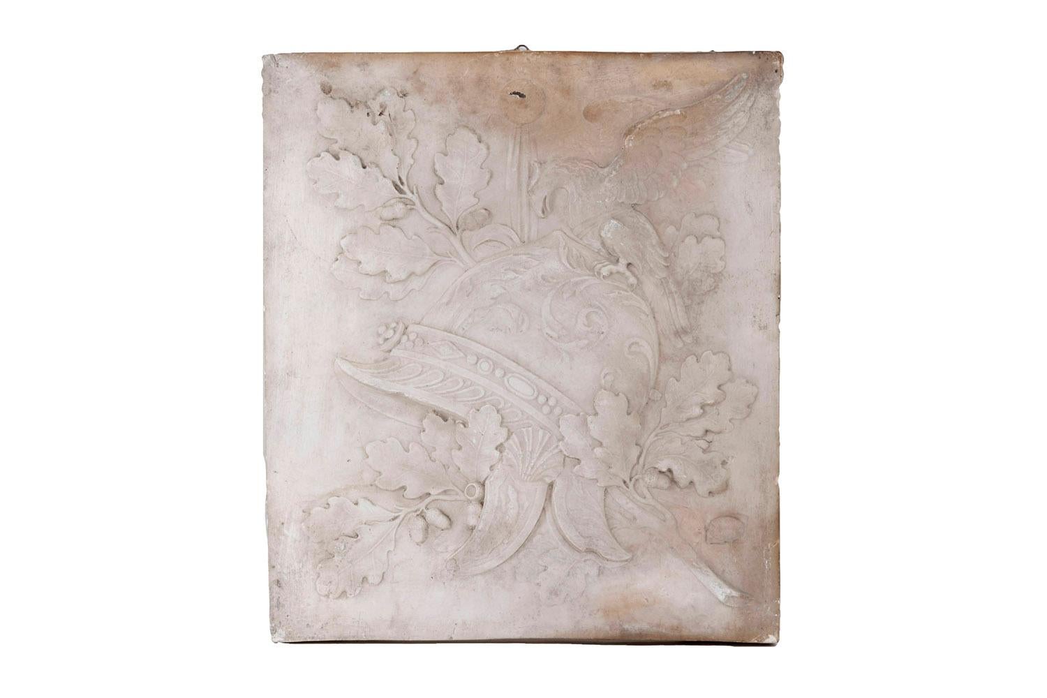 Stucco low-relief figuring the Victory allegory. Military helmet central motif adorned with foliar ornaments, gadroons, shell and salamander. It’s crowned with an eagle and rests on oak branches, leaves and acorns.
Hollow stamp on the bottom right