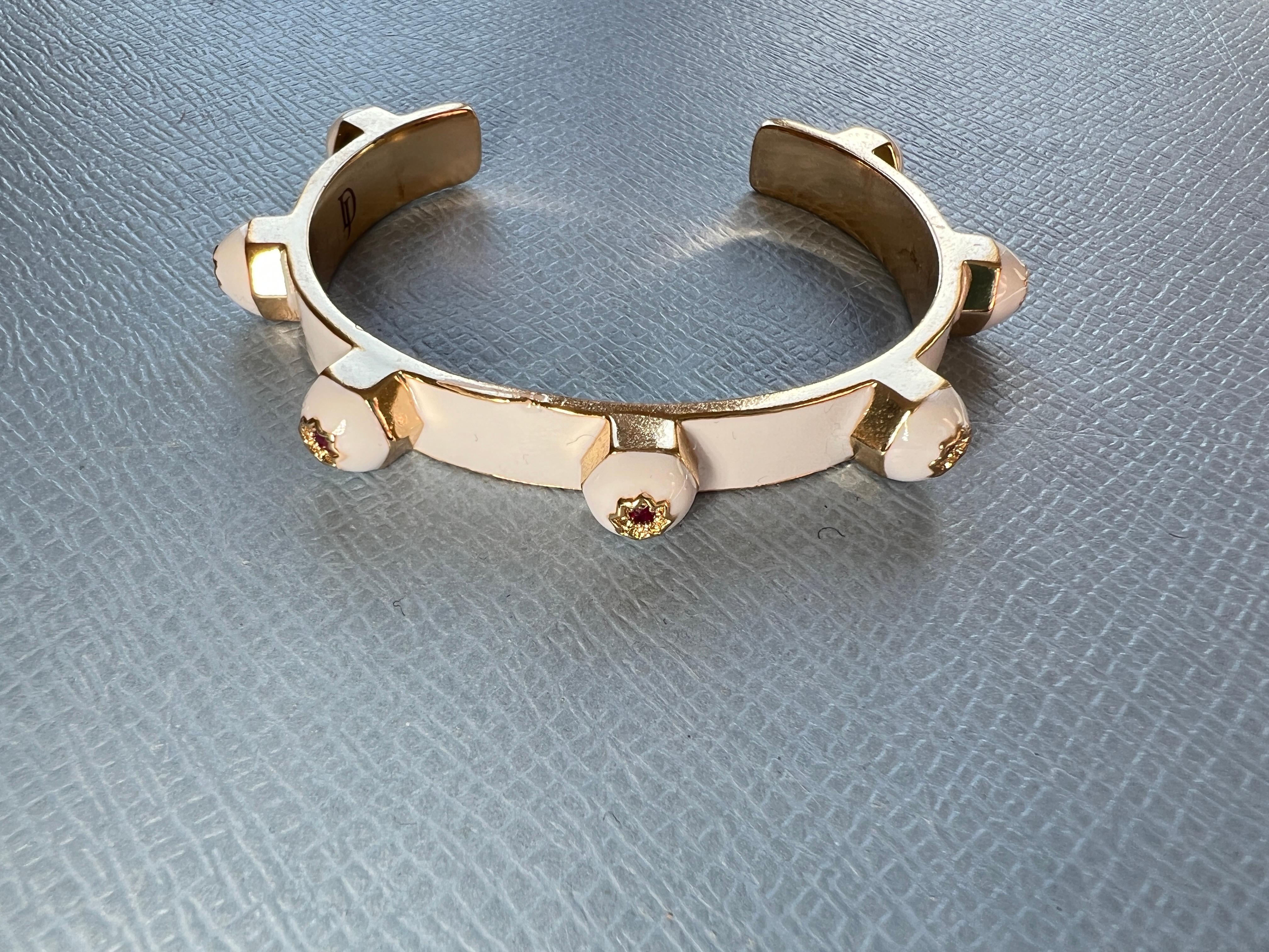 Ce bracelet manchette moderne en plaqué or de J Dauphin est orné de sept rubis, chacun serti dans une étoile sculptée à huit branches, et se termine par des détails en émail blanc lisse. Cette pièce allie un style percutant à une profondeur
