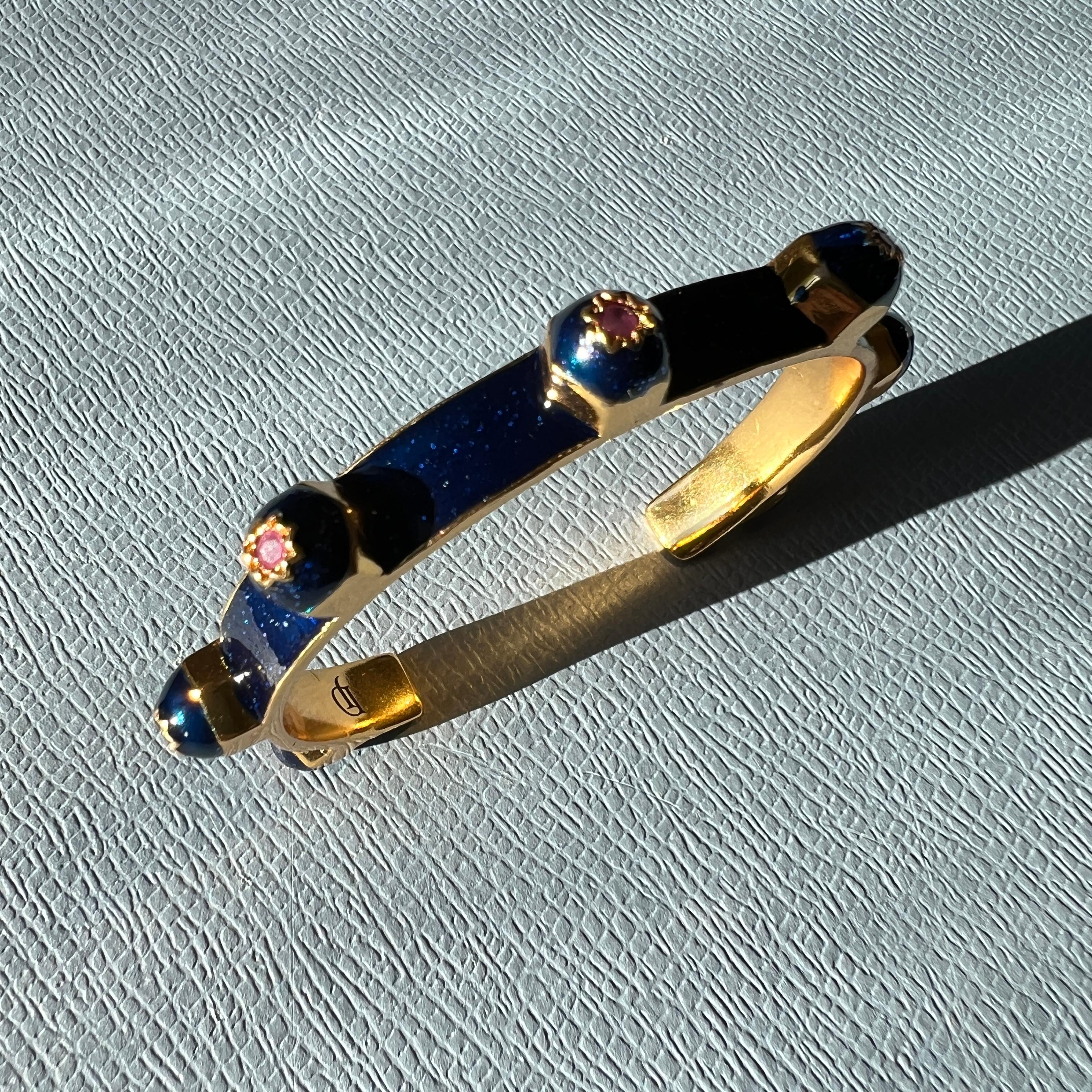 Questo bracciale largo di J DAUPHIN è realizzato in ottone placcato oro 18 carati, rifinito con smalto glitter blu intenso e dotato di sette rubini naturali incastonati in motivi a otto punte. Progettato come uno scultoreo bracciale aperto, il pezzo