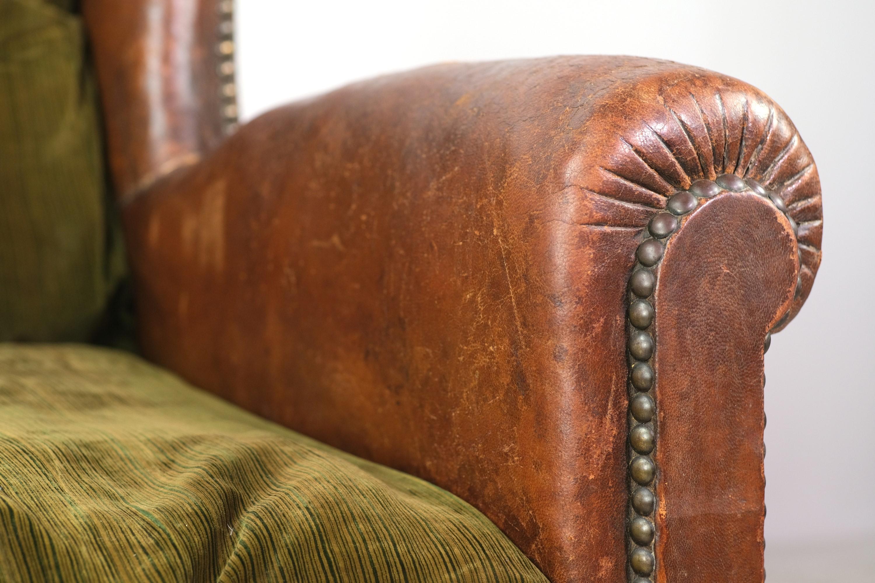 European brown leather club chair with green stripped velvet seat cushion. It features brass nail head studs detail all along the frame and has a warm natural patina. Adding to the style are round wood legs in the front. There is expected wear from