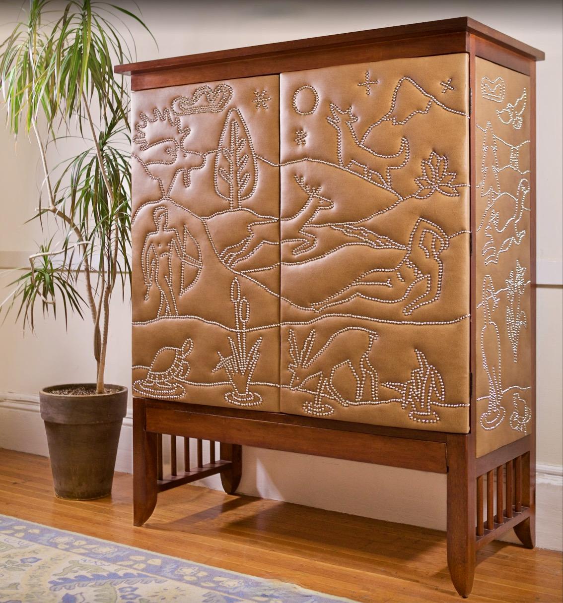 Vintage walnut cabinet with two doors and side panels of brown leatherette artistically decorated with small chrome head tacks representing various native flora and fauna of New England, including beaver, moose, turtle, wolf, deer, bear, fox,