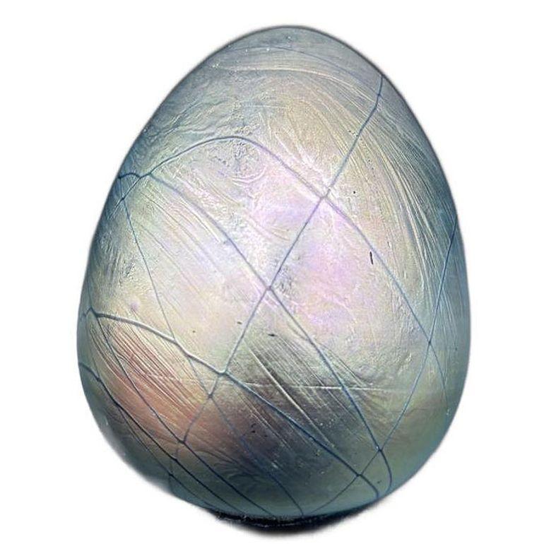 This Maslach signed studio art glass paperweight, dated 1979, features an elegant egg shape with a stunning iridescent surface that shimmers in hues of deep blue, soft green, and warm gold. Its smooth, modern design makes it a striking accent for
