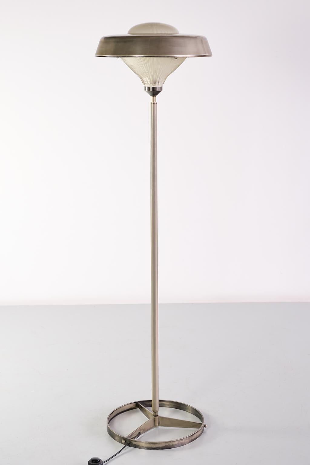 This rare floor lamp was designed by Studio BBPR and produced by Artemide, Italy in 1962. The striking design consists of a circular base in nickel plated steel with three parts leading to the central tubular steel stem. The shade is made of reeded