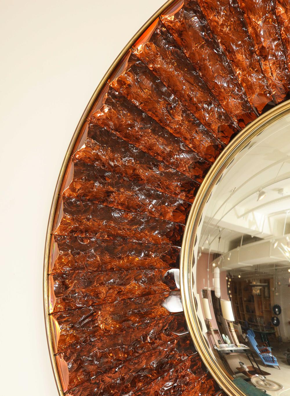 Hand-cut & chiselled slabs of burnt orange colored crystal surround a central, circular convex mirror.  Oxidized brass surround and mount. Signed on outer edge.