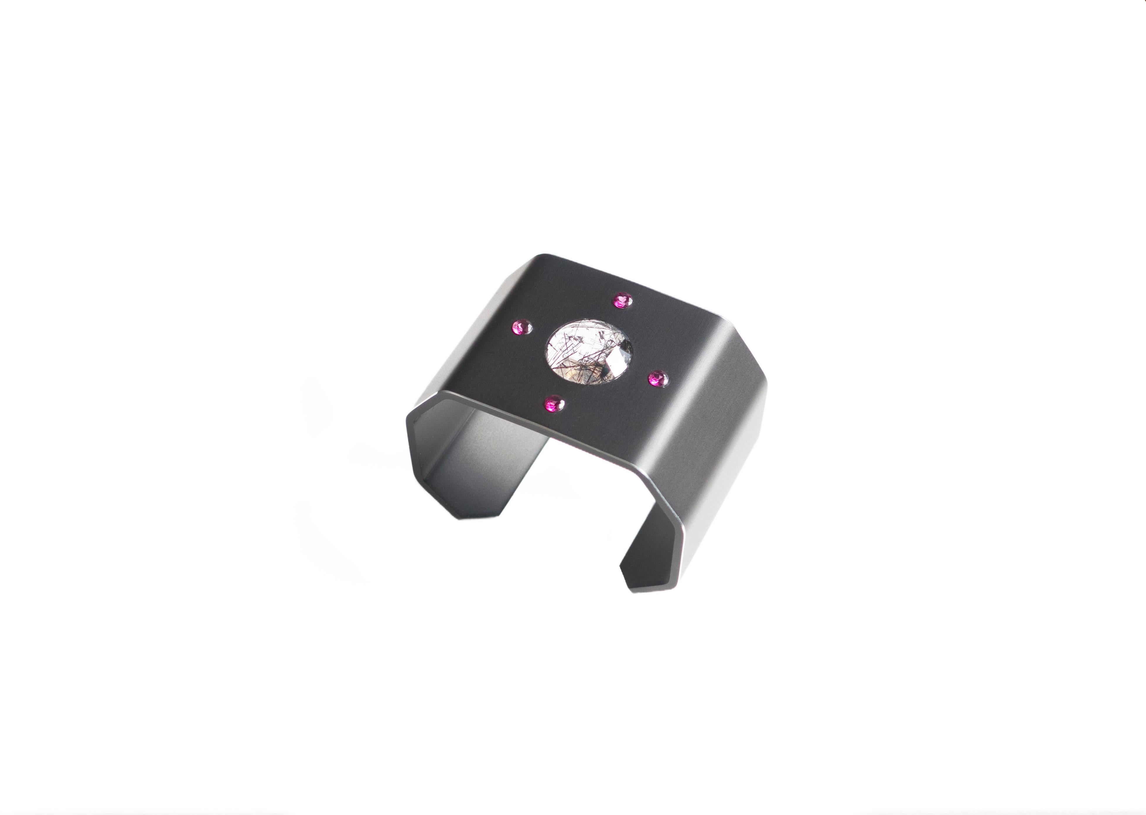 Mirus cuff by Studio C at Second Petale Gallery

This highly modern and graphic cuff is made up of black anodised aluminium. It is adorned with a rose-cut tourmaline-quartz, custom-made by a French stone-cutter
and four small rhodolite