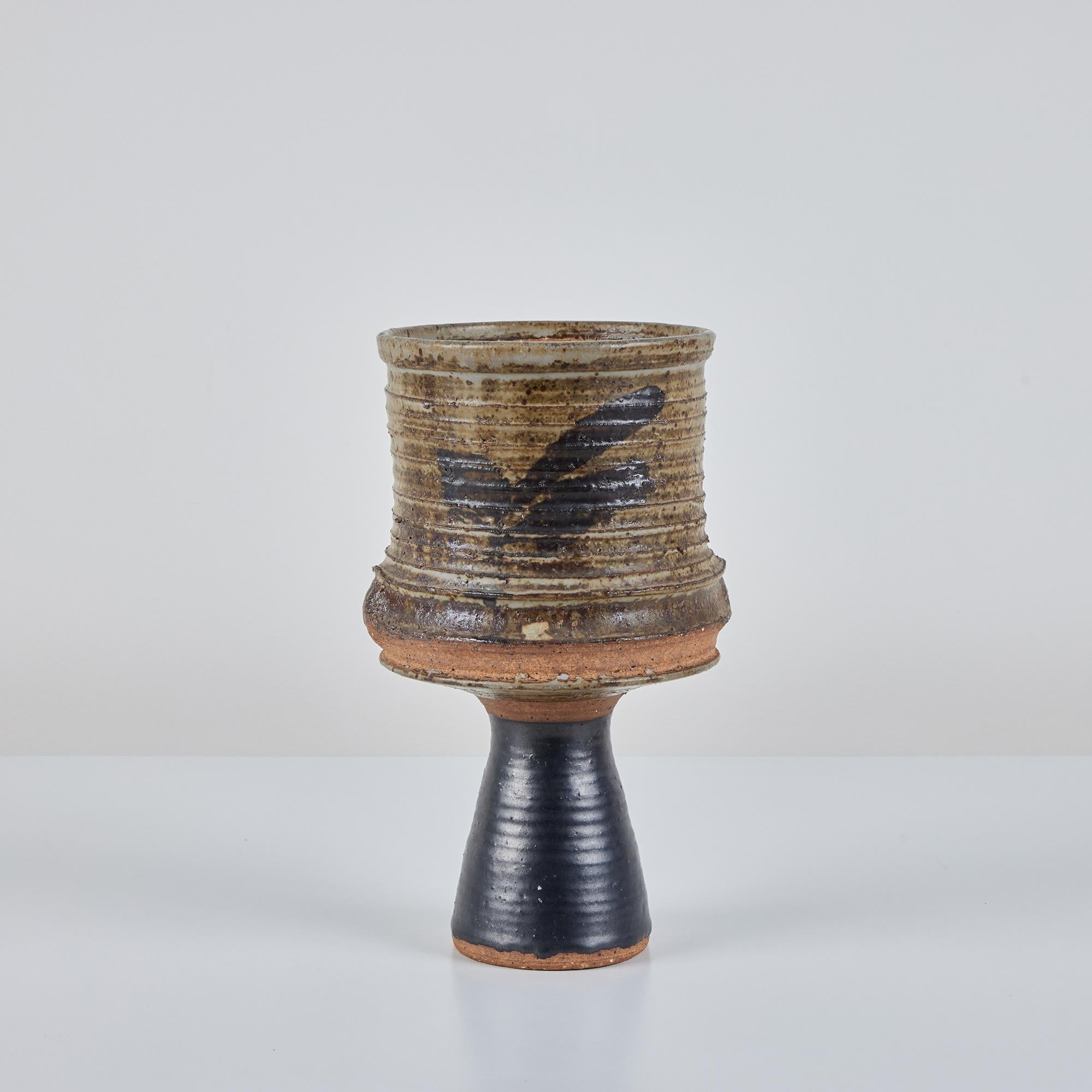 A tall, stoneware ribbed cylindrical vase with imperfect forest green glaze on the body's ribbed portion. This would easily fit in sitting empty on a shelf as a decorative object, or full of flowers on a credenza . Containers like these, with a