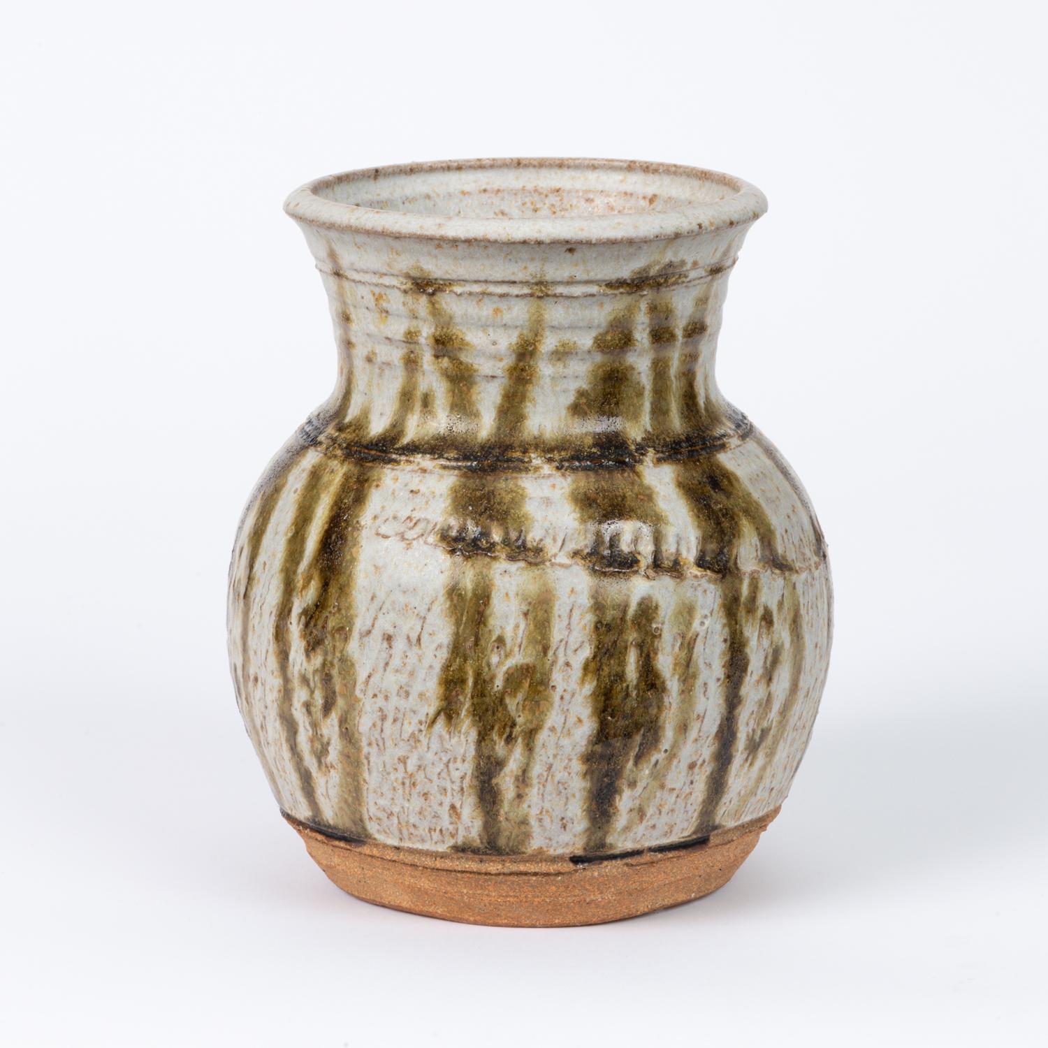 A Studio Pottery ceramic vessel in glazed stoneware. The pieces features a khaki colored glaze with vertical dark green striation, while the bottom and lower portion is left unglazed in the natural stoneware clay. Signed by artist on