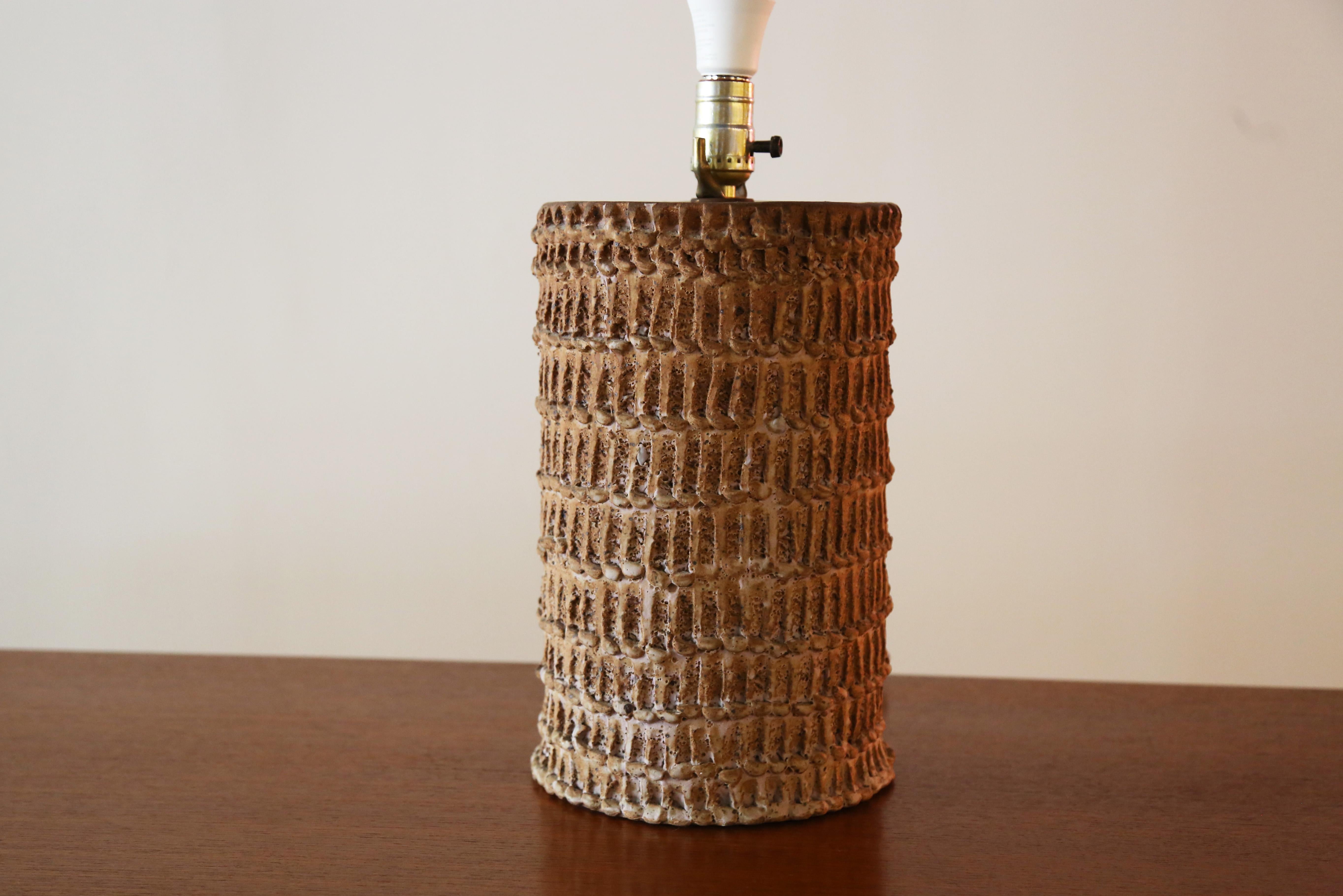 A vintage studio ceramic table lamp with a great squatted presence. The surface with repeated sgraffito scrapes around the entire surface lends a great texture and visual appearance to the lamp. The surface of the lamp incised with the signature