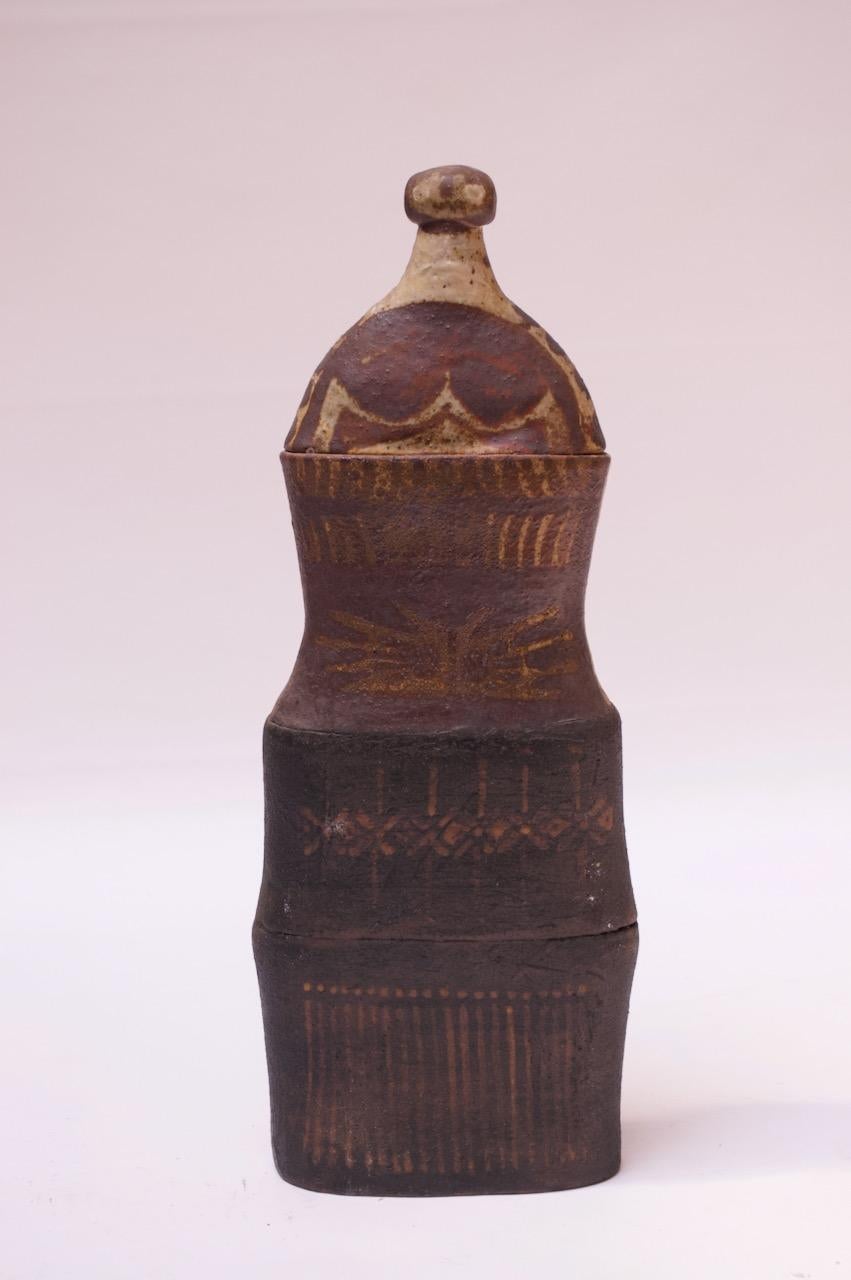 1970s tall studio terracotta jar / urn, uniquely thin with a removable lid. Hand-applied linear and geometric design with an attractive color palette of black, brown, beige, and red. 
Crude by design, the lid fits very snugly on the top (difficult