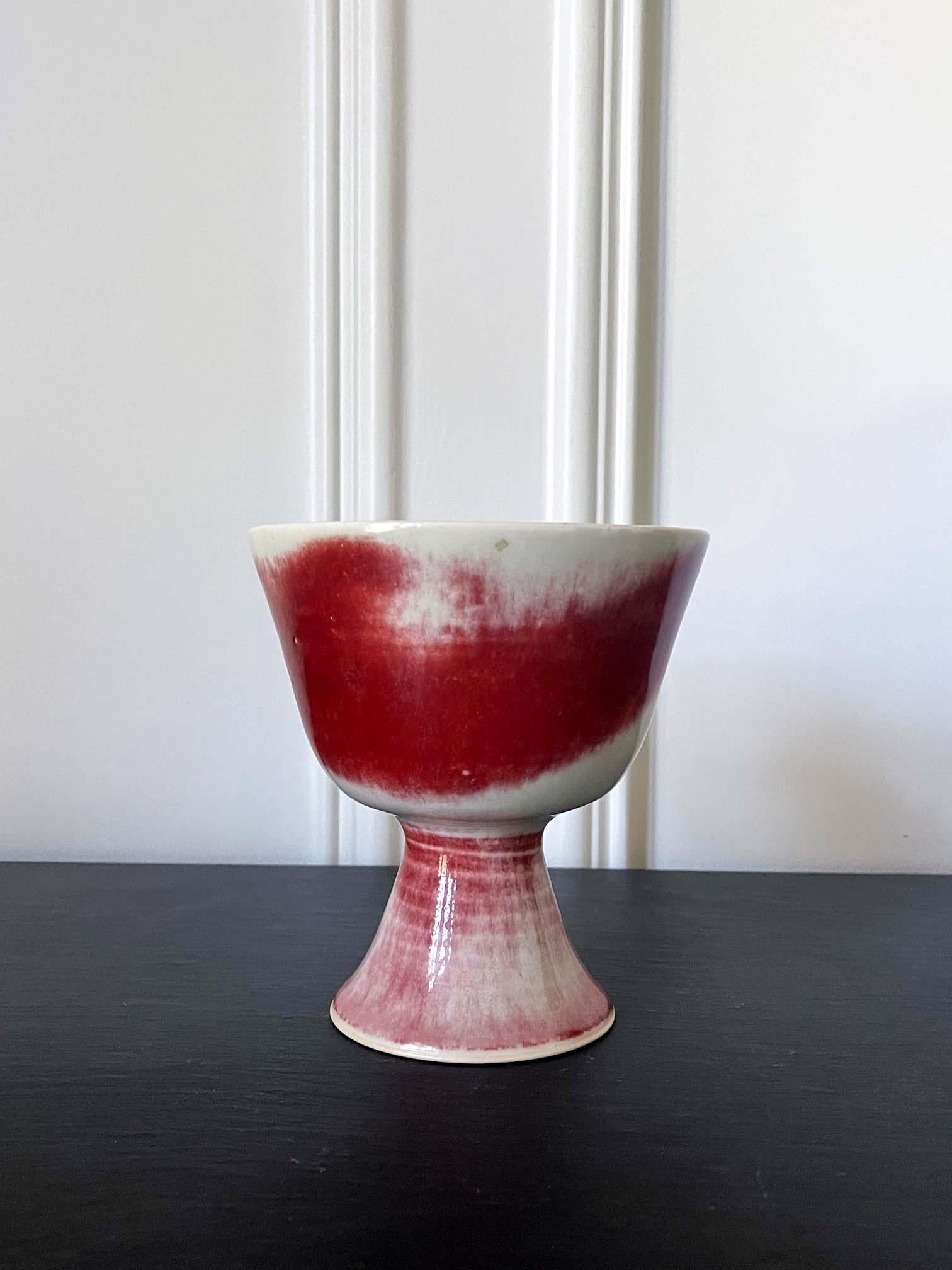 Ein Keramikgefäß in Form einer Schale oder eines Kelches mit Fuß, hergestellt im Studio von Bruder Thomas Bezanson (1929-2007) um die 1970er Jahre. Die Schale ist mit einer leuchtenden roten Freiformglasur auf weißem Grund überzogen und hat ihre