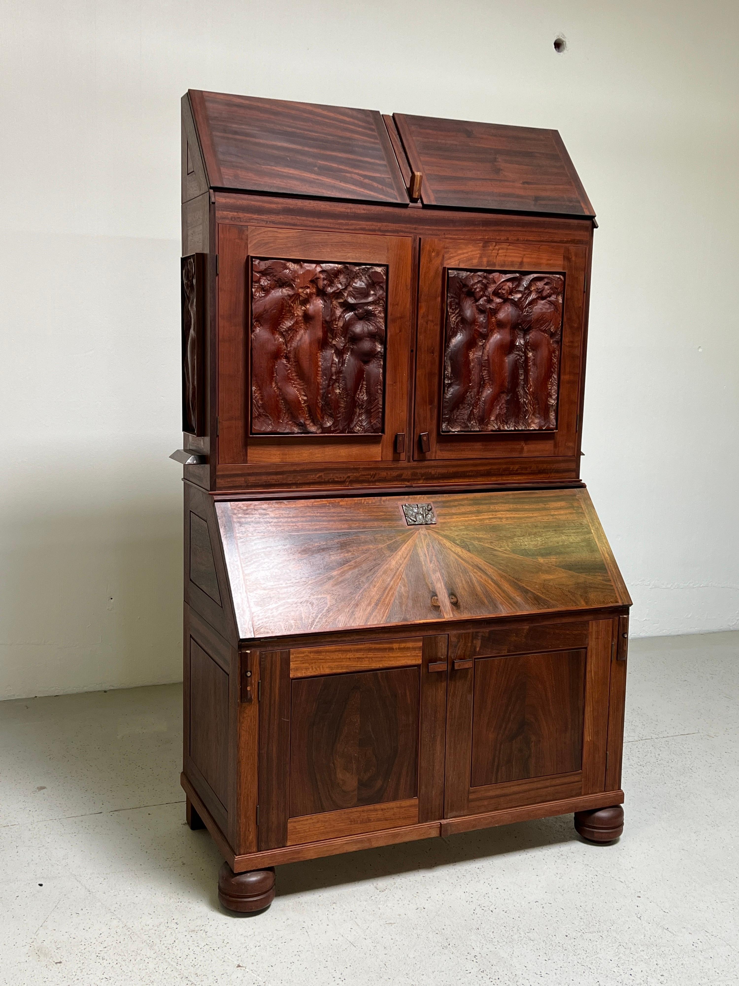 An incredibly crafted drop front secretary desk by Karel Mikolas. Made from various solid hardwoods with carved panels and a cast bronze key escutcheon.