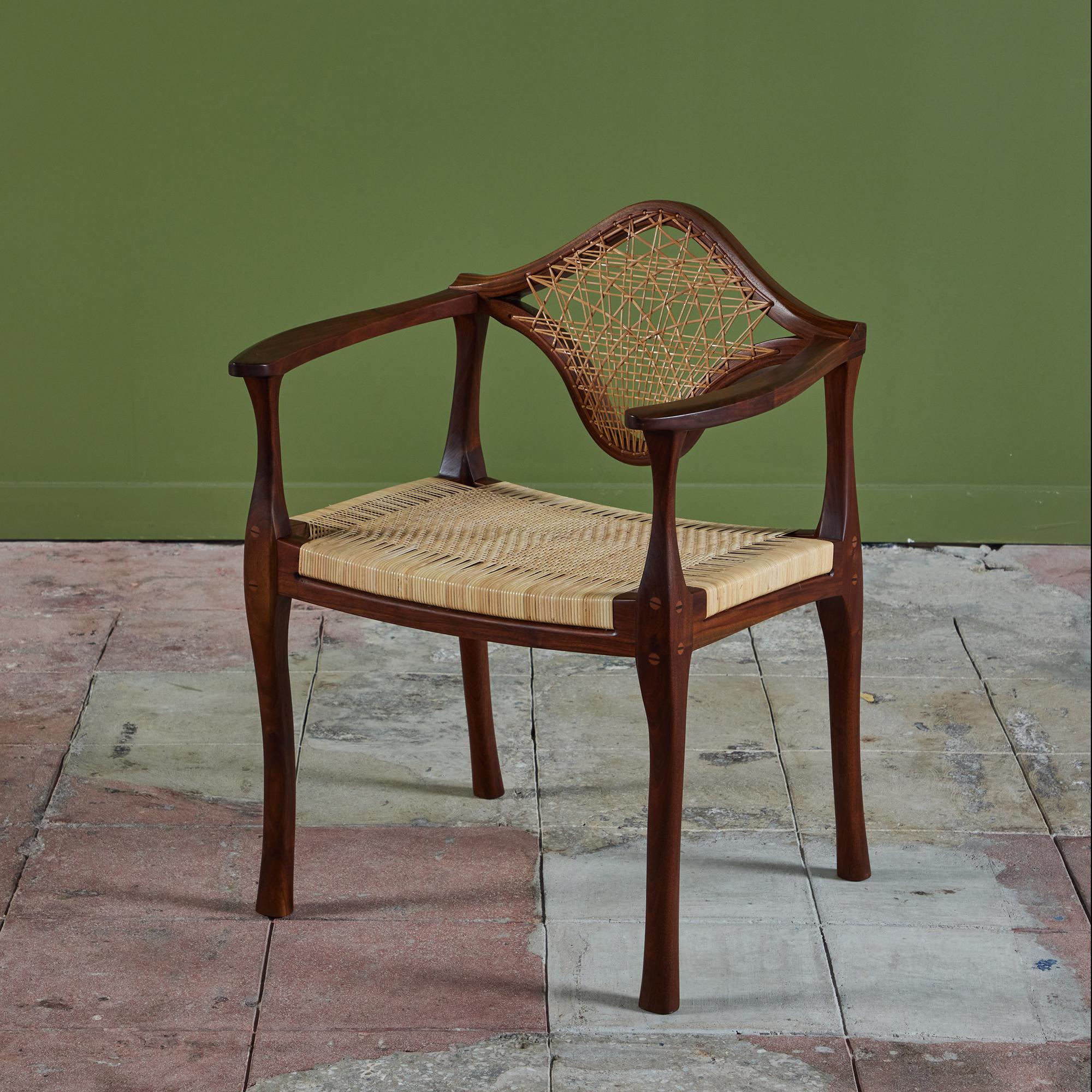 A walnut studio craft arm chair c.1983 is truly one of a kind. The chair features a sculpted wood frame with soft curves and cascading legs. The seat-back showcases the original uniquely woven cane while the seat has been newly caned.  Underside is