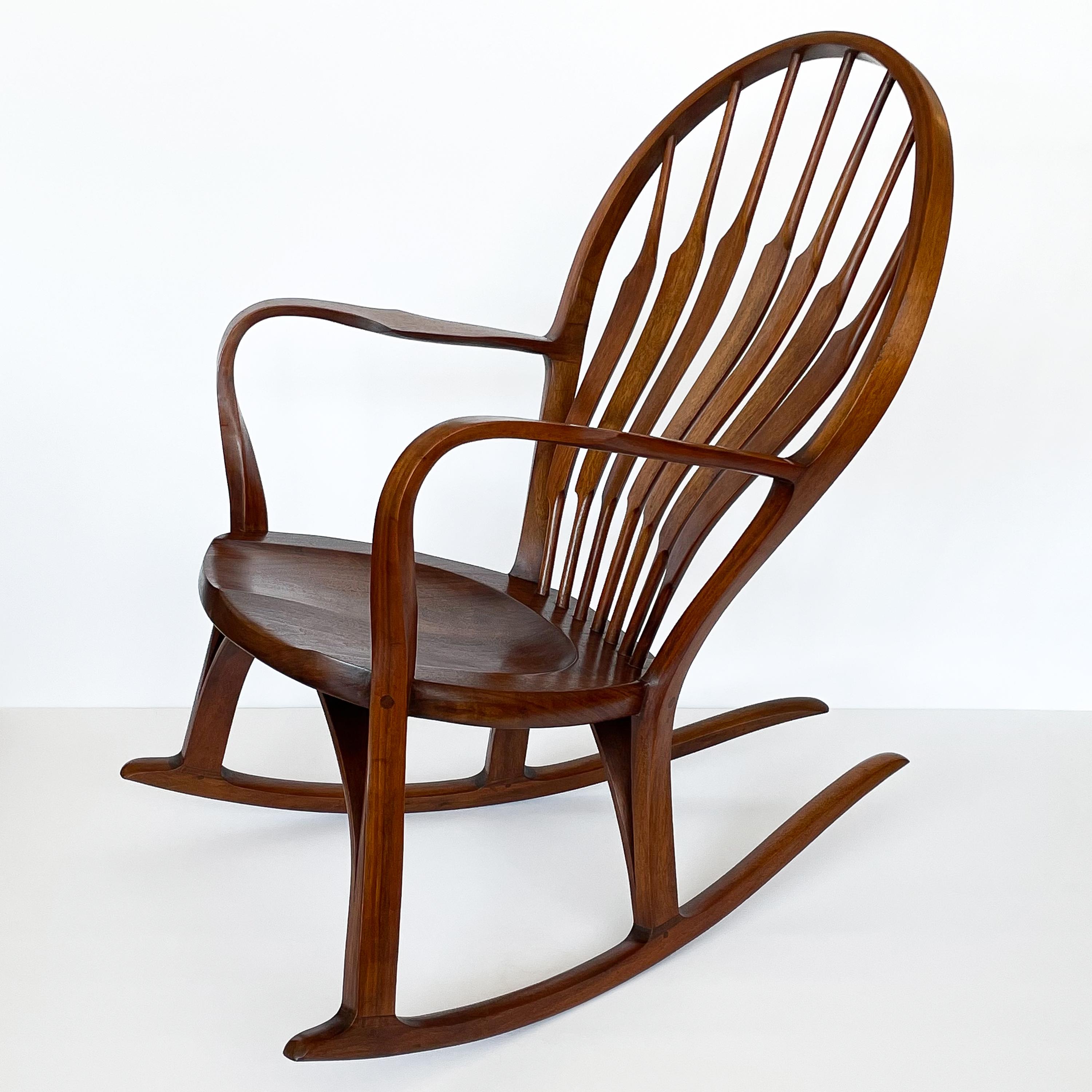 A sculptural handmade American studio craft walnut rocking chair by Steven Foley, circa 1978. This rocking chair features a horseshoe shaped back with 6 sculpted hand carved curved slats that is reminiscent of a Wegner peacock chair. Long curved
