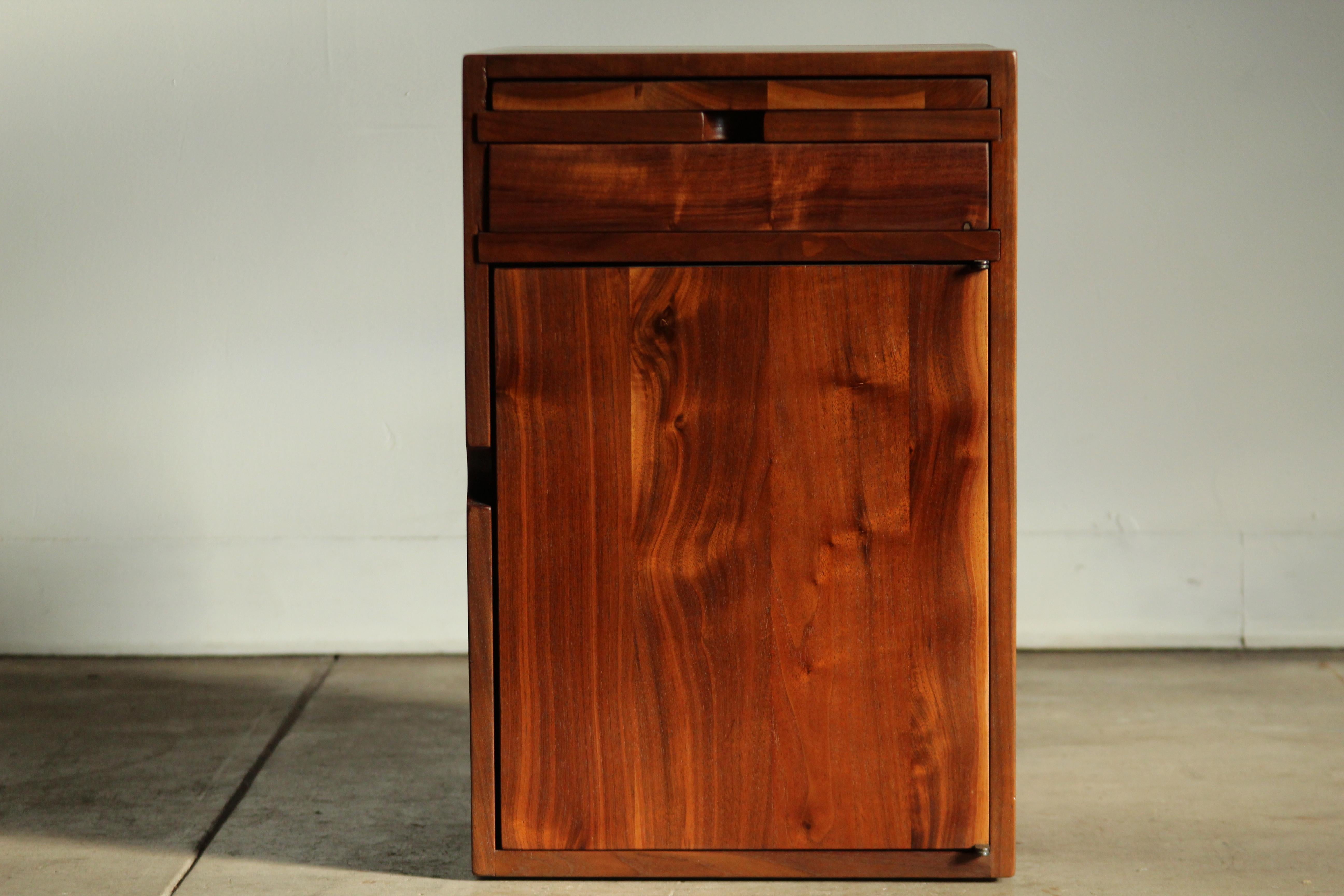A stunning, studio crafted end table constructed of solid Claro walnut, made by an unknown designer in the 1970s. The table features a large storage area, a small drawer and a pull out tray for a drink, book, bong, etc. This piece has been lovingly