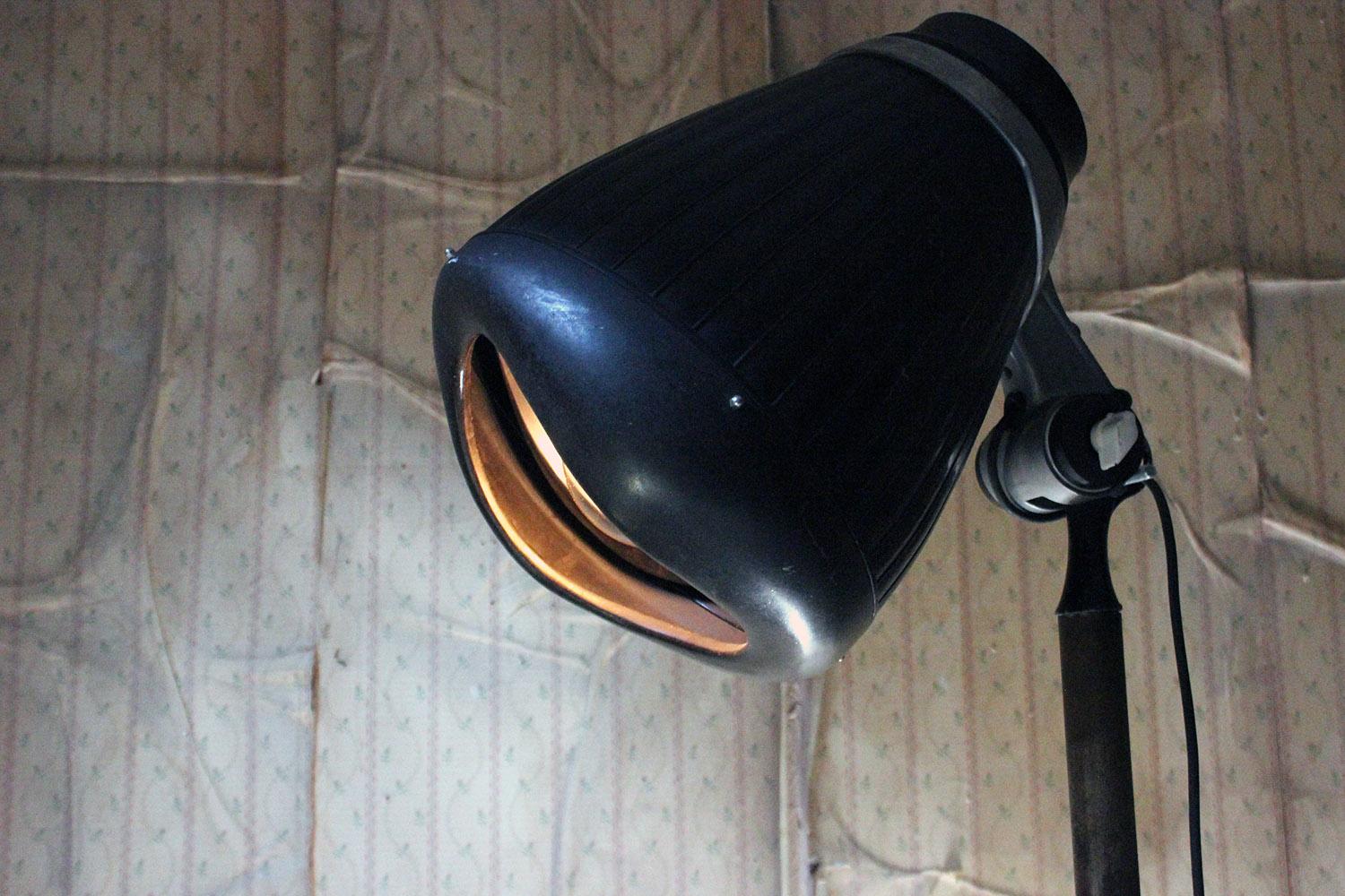 The tubular metal and large hooded heavy duty dryer, now converted to a studio floor lamp, to an adjustable column and a four legged base with industrial castors and the makers name for Eugene Ltd, the on/off switch now working as a lamp switch, and