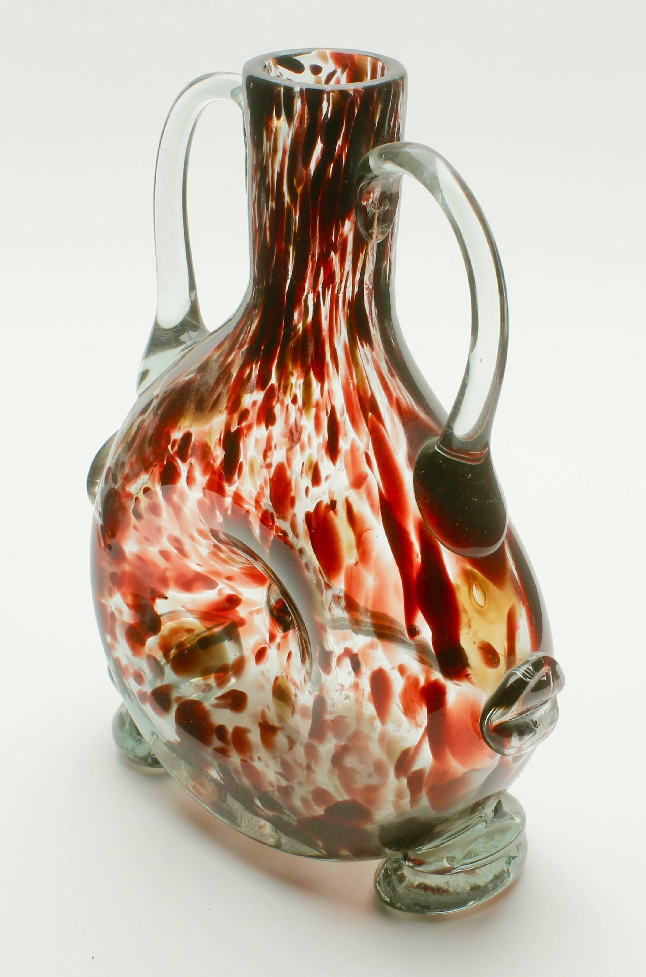 Studio glass vase based on a mouth-blown bottle shape of tortoise-shell splatter pattern (in red/brown), indented in the centre and clear glass used for hand-applied handles, feet and side-details. It has a rough pontil on the bottom and no visible