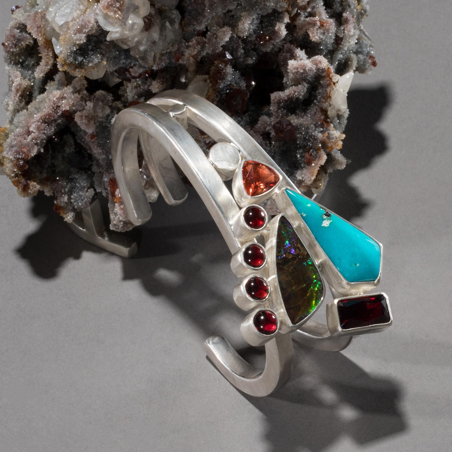 Turquoise cuff on sphalerite with garnet

The arrow-like shape of a piece of sky-blue turquoise sets the tone for Studio Greytak’s Turquoise Cuff on Sphalerite with Garnet. Beside the powerful warrior stone, turquoise, sit iridescent ammolite and